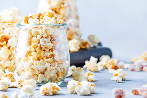 Caramel sweet popcorn in glass jars, gray background, selective focus