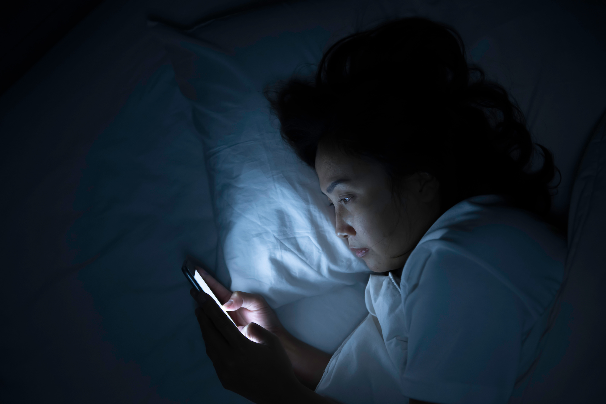 Woman plays with  smartphone in bed at night, (CNN)...