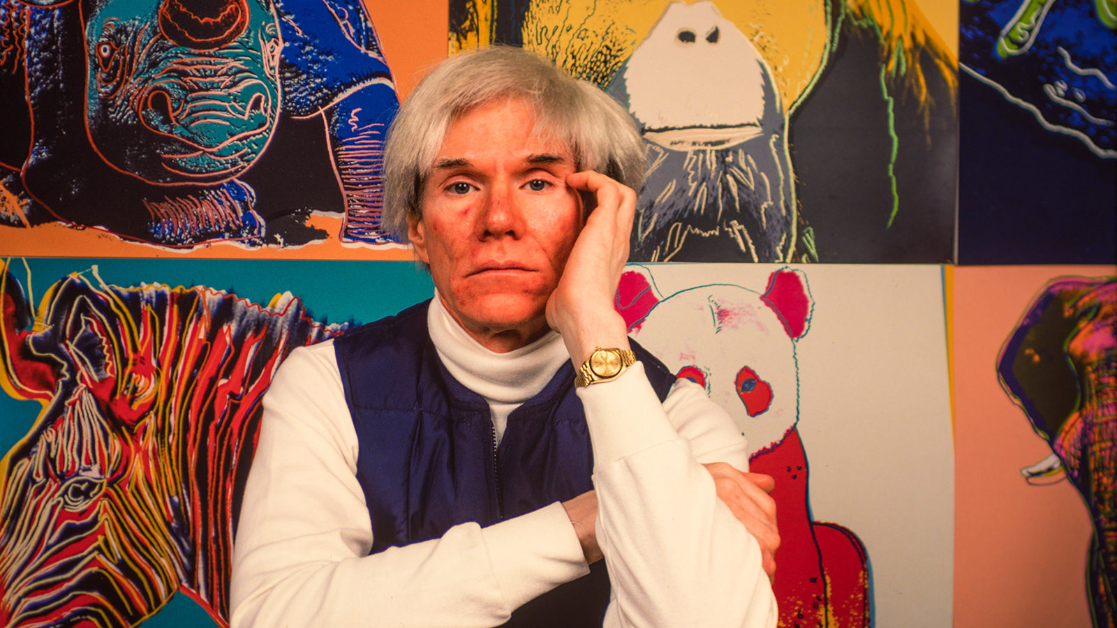 American Pop artist Andy Warhol (1928 - 1987) sits in front of several paintings in his 'Endangered...