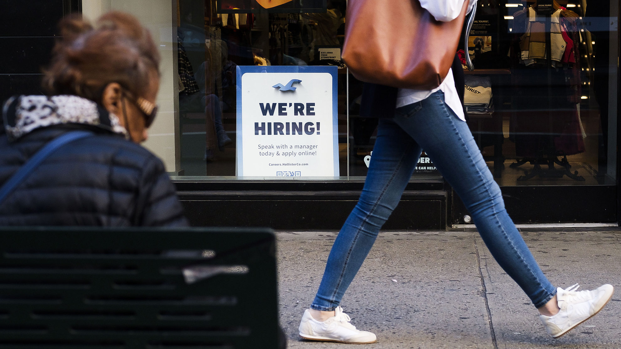 a person walks past a "hiring" sign...