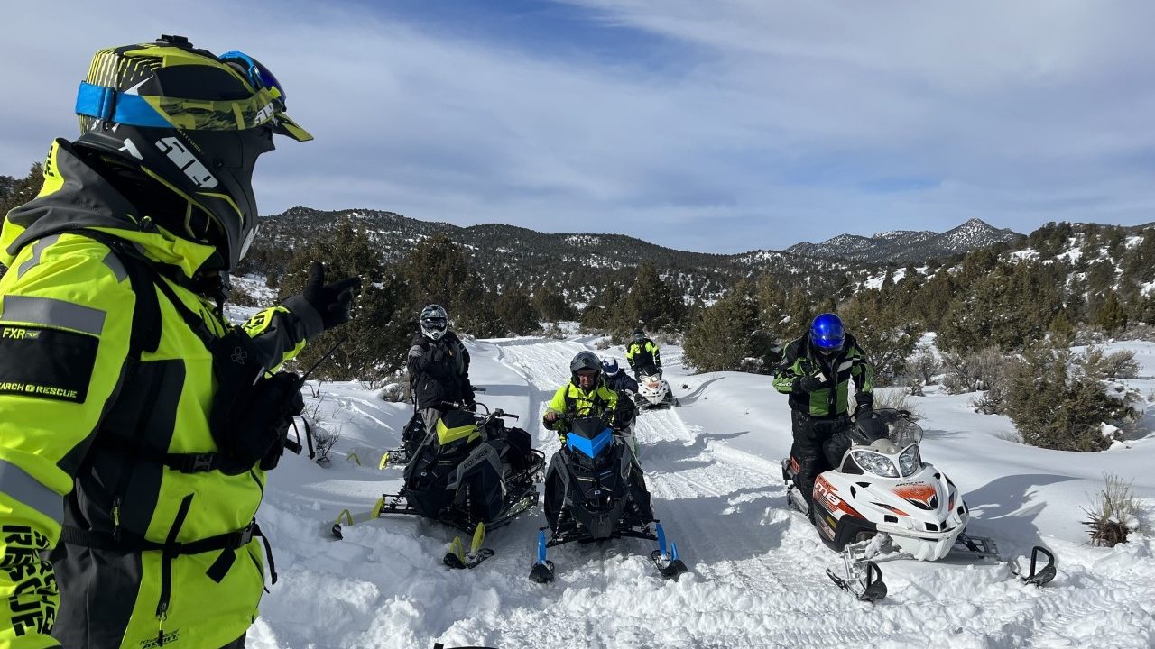 Six rescuers, each on a snowmobile, are pictured...