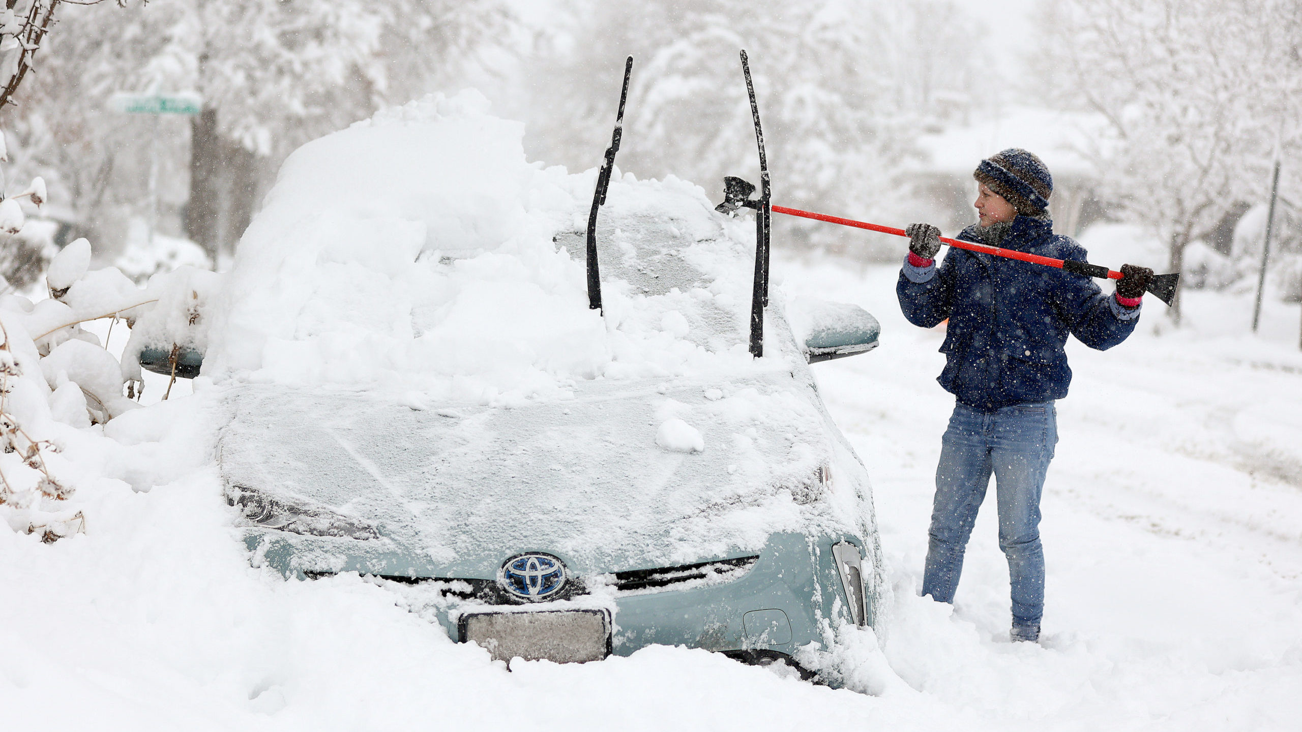 a woman cleans off snow from her car after utah snowstorm...