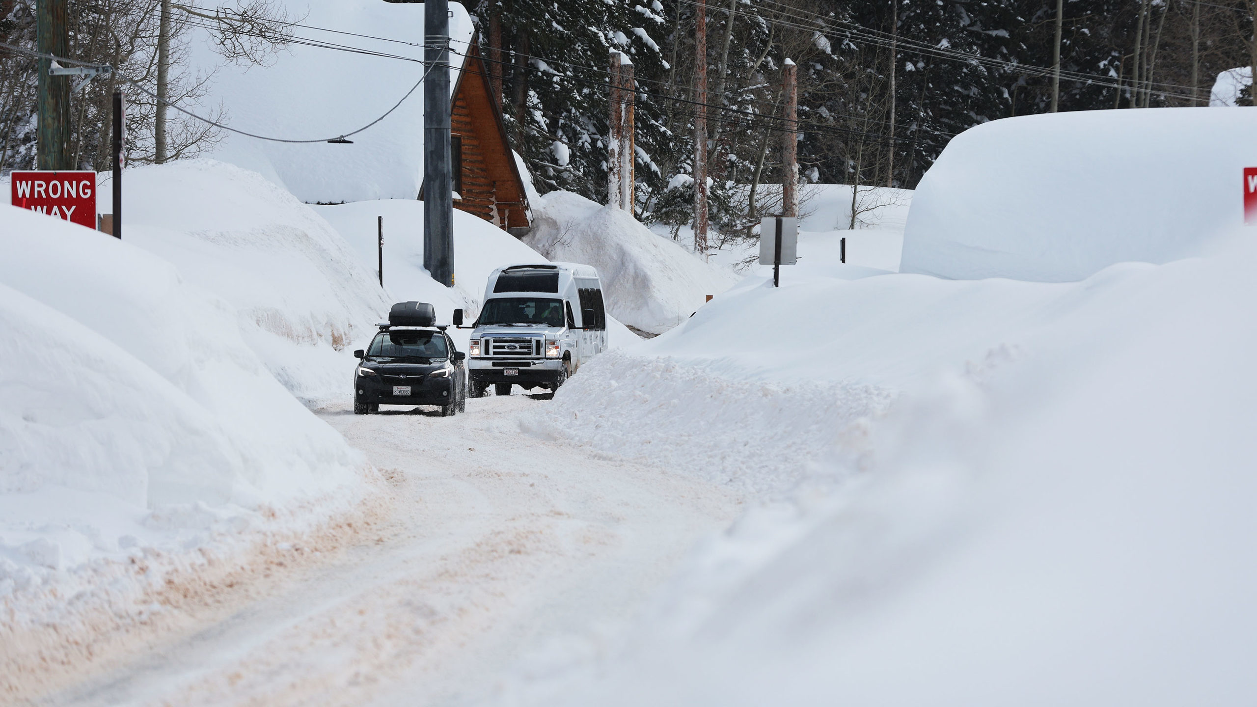 cars drive through piled up snow on road...