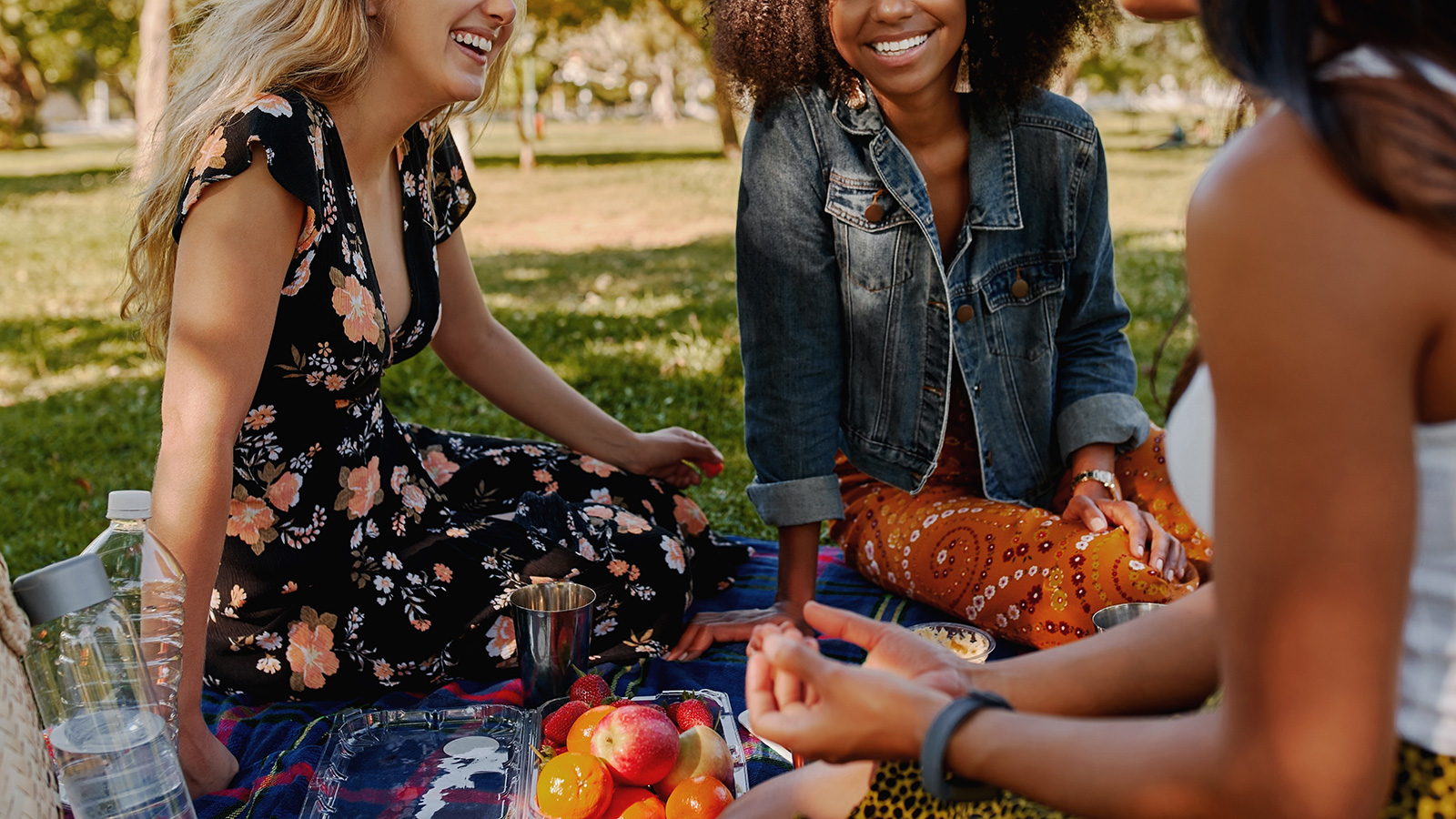 Smiling multiracial female friends having fun at picnic in the park - group of healthy friends havi...