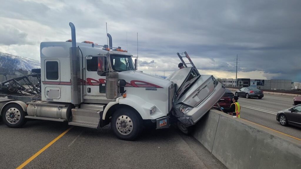 the crash in kaysville is pictured, a semi is pinning a car to a barrier...