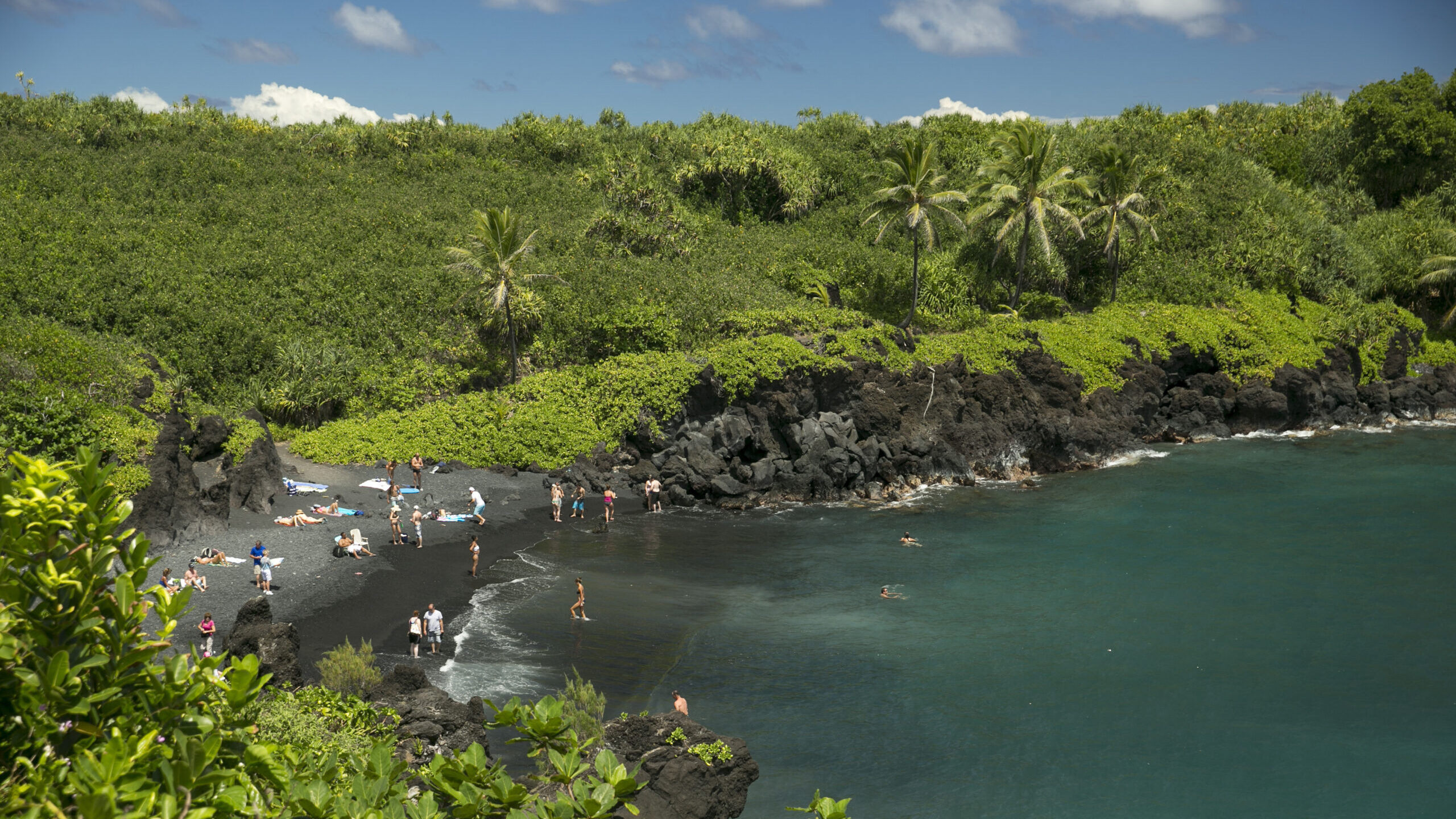 FILE - People spend time on the black sand beach at Waianapanapa State Park in Hana, Hawaii, on Sep...
