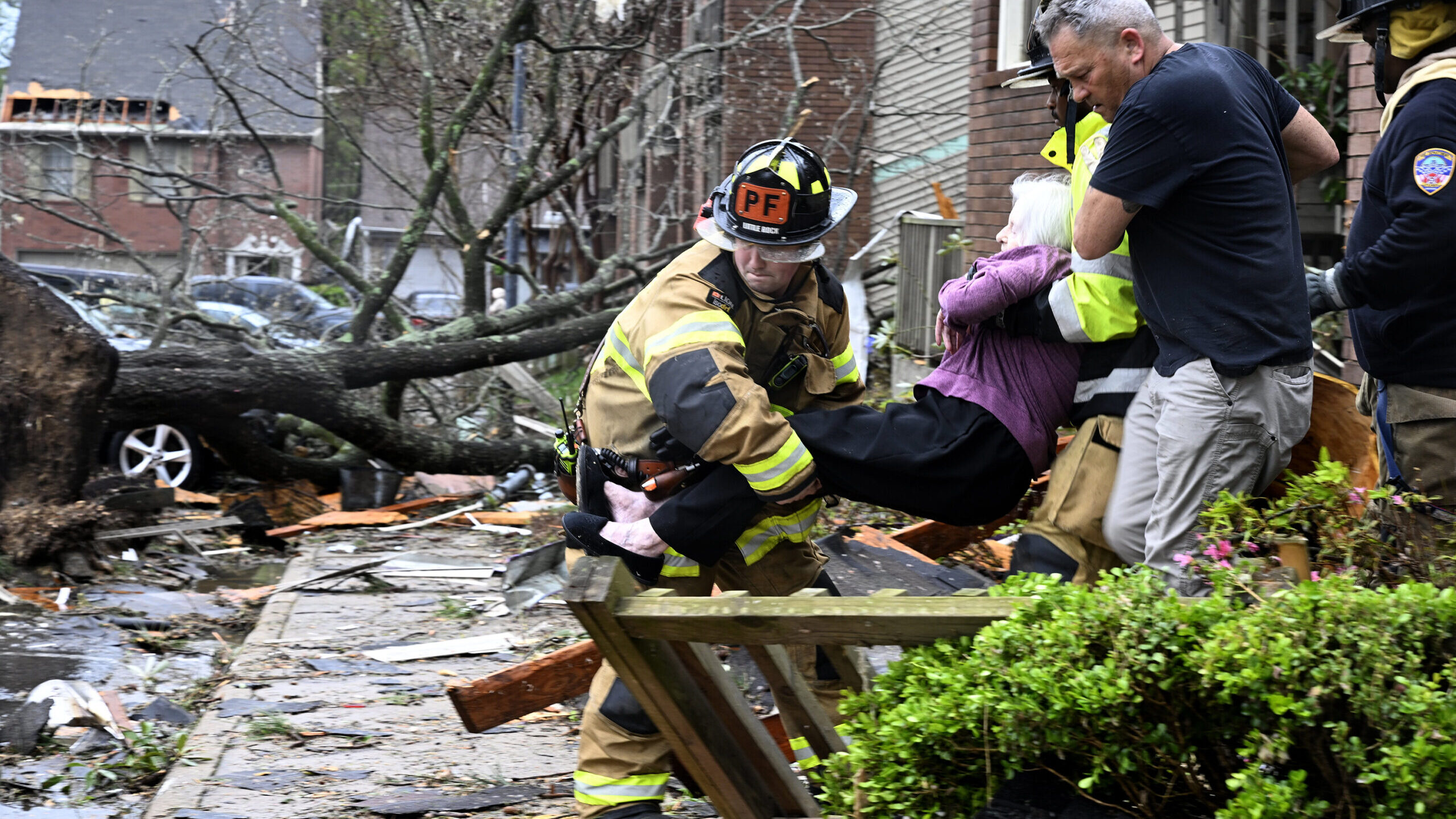 Firefighters carry a woman out of her condo after her complex was damaged by a tornado on Friday in...