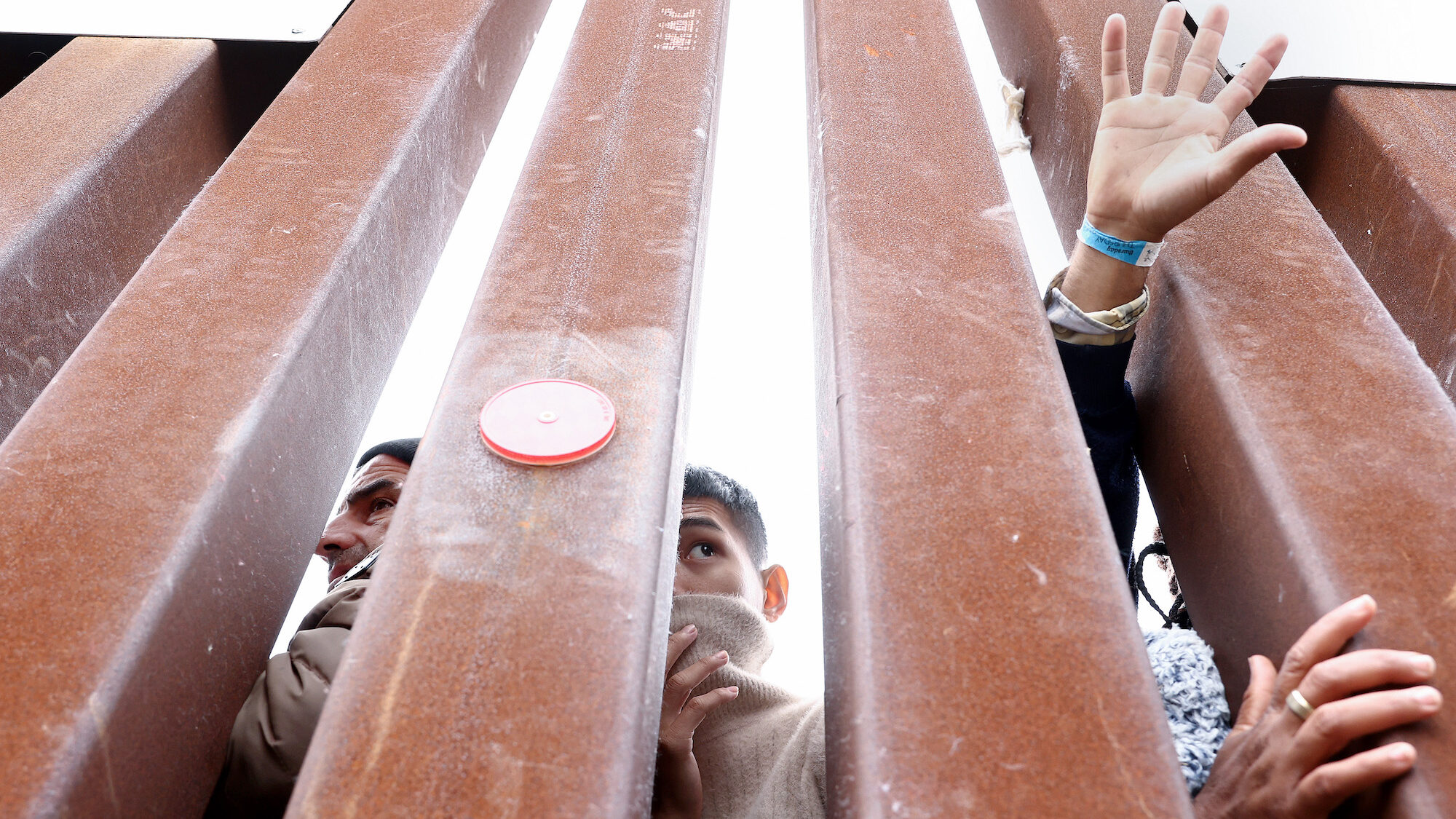 Migrants seeking asylum in the US look through the border wall as volunteers offer assistance on th...