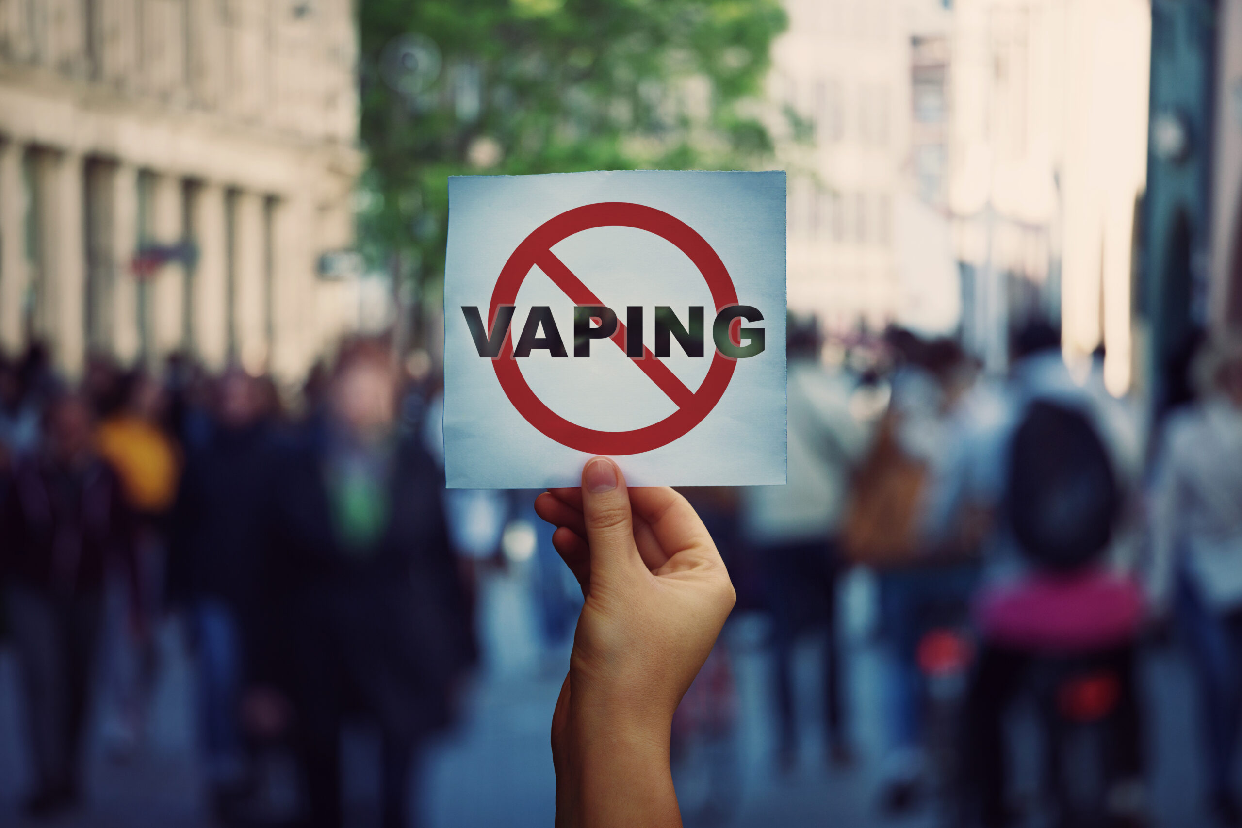 Human hand holding a protest banner stop vaping message over a crowded street background....