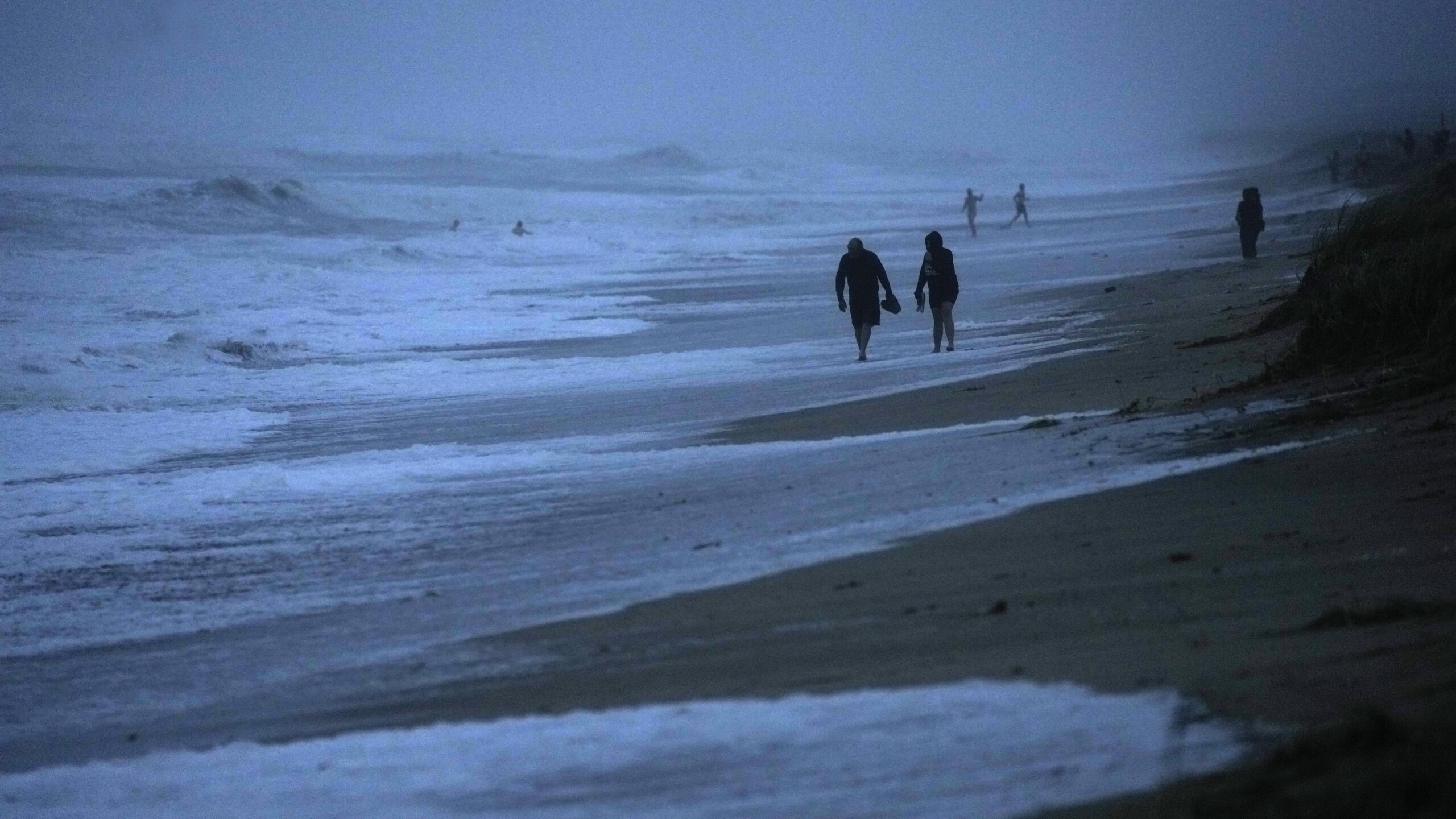 FILE - People walk along the oceanfront at Jensen Beach Park, where waves were reaching the dune's ...