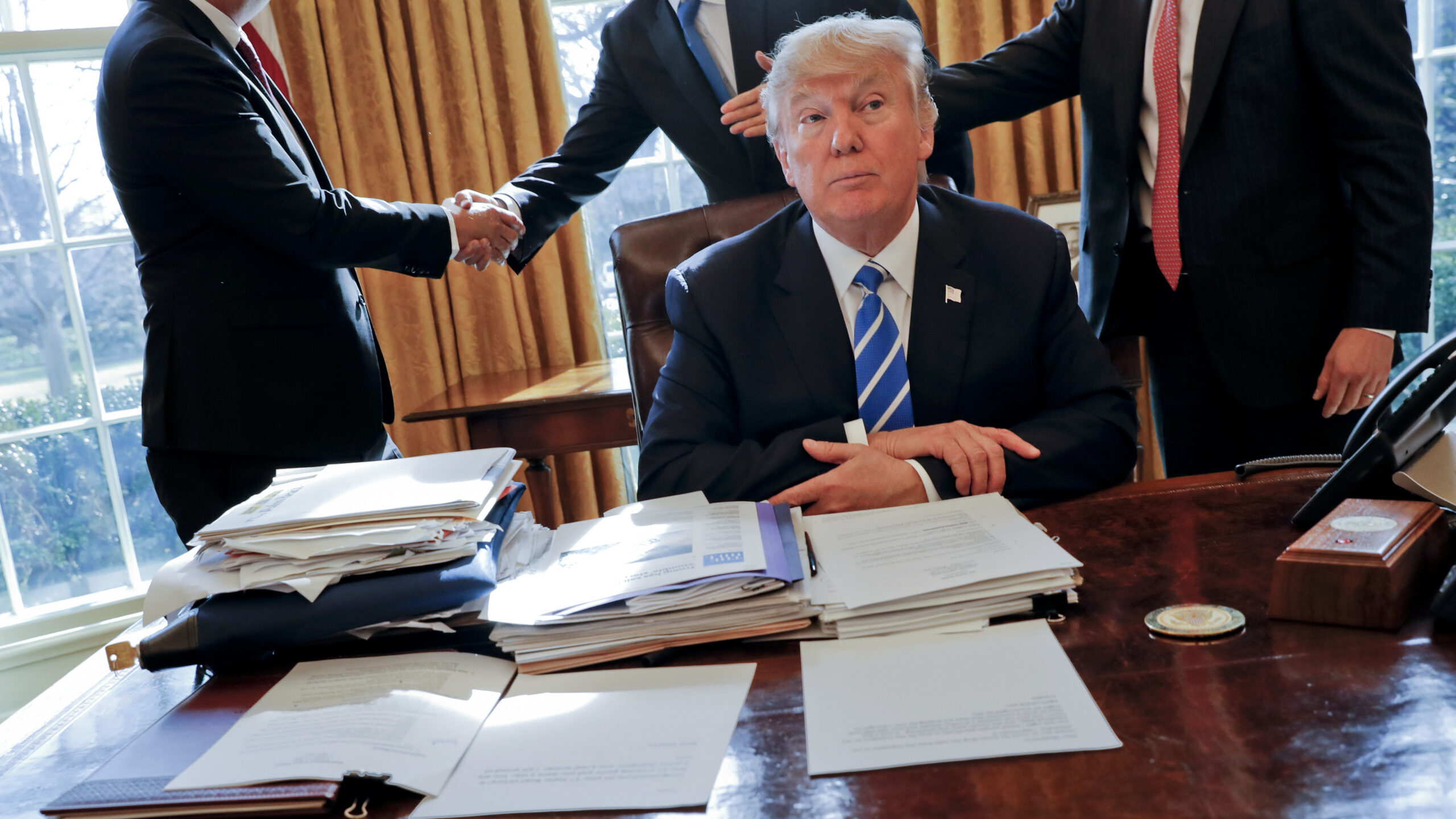 FILE - President Donald Trump sits at his desk after a meeting with Intel CEO Brian Krzanich, left,...