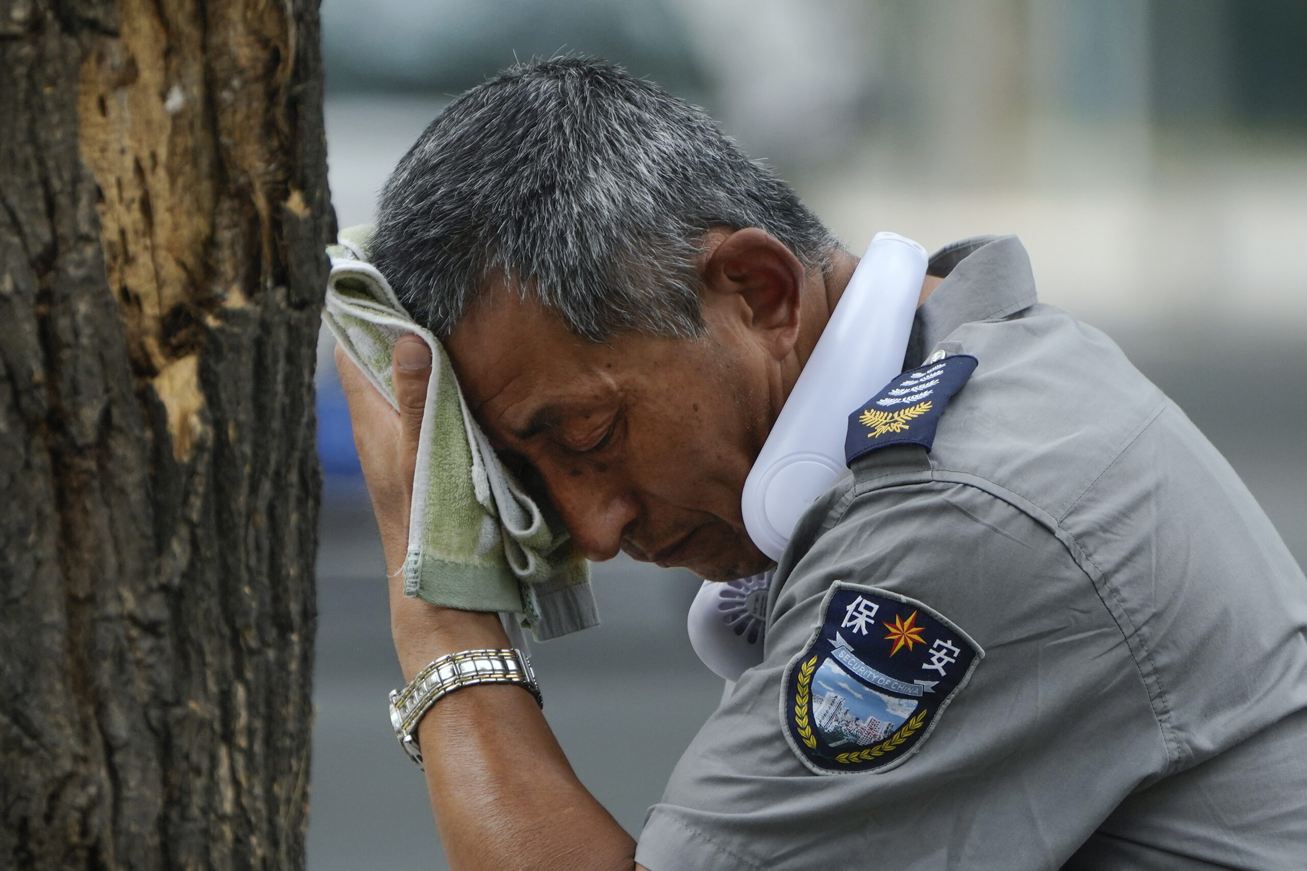 A security guard wearing an electric fan on his neck wipes his sweat on a hot day in Beijing, Monda...