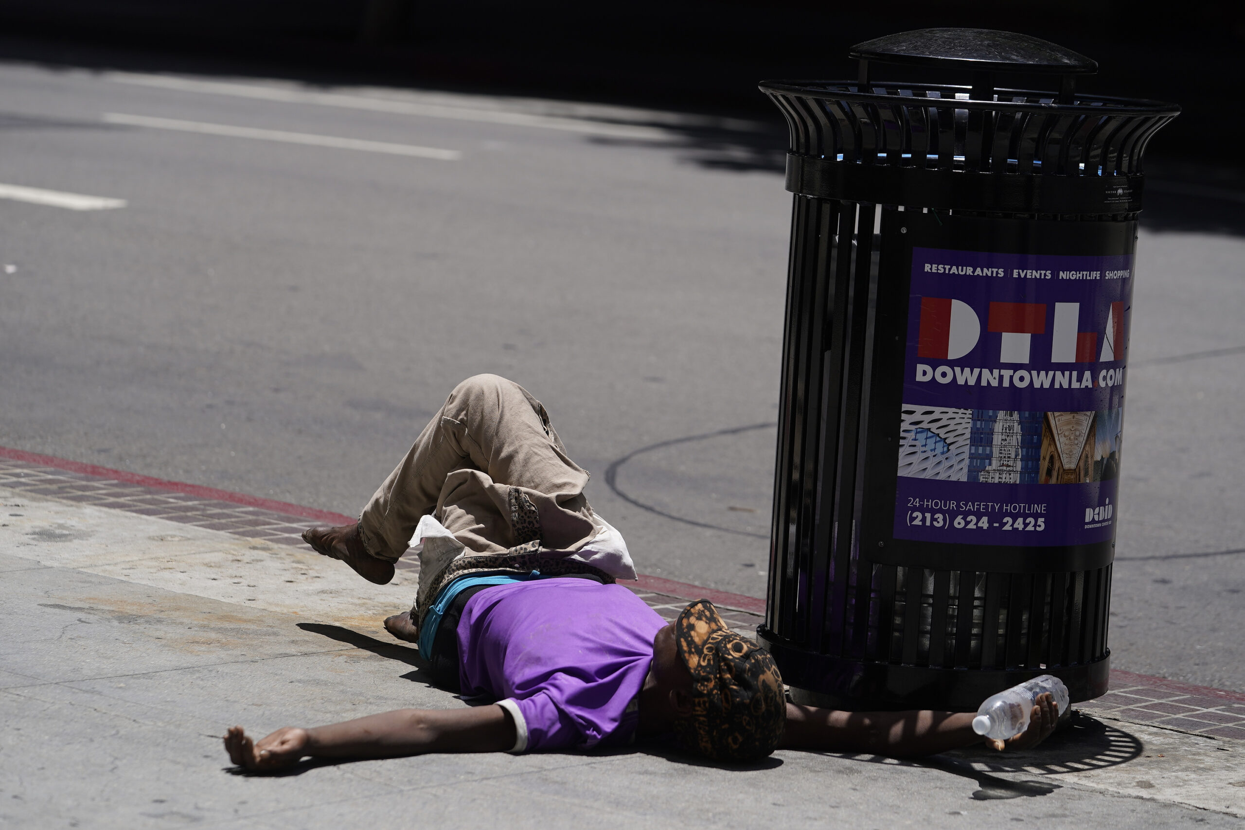 FILE - A homeless person lies on the sidewalk while holding a water bottle, Sunday, July 2, 2023, i...