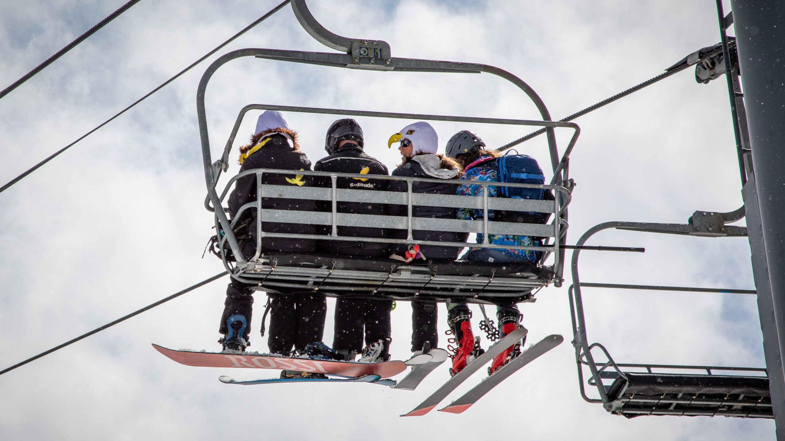 Skiers and snowboarders are seen riding on a ski lift....