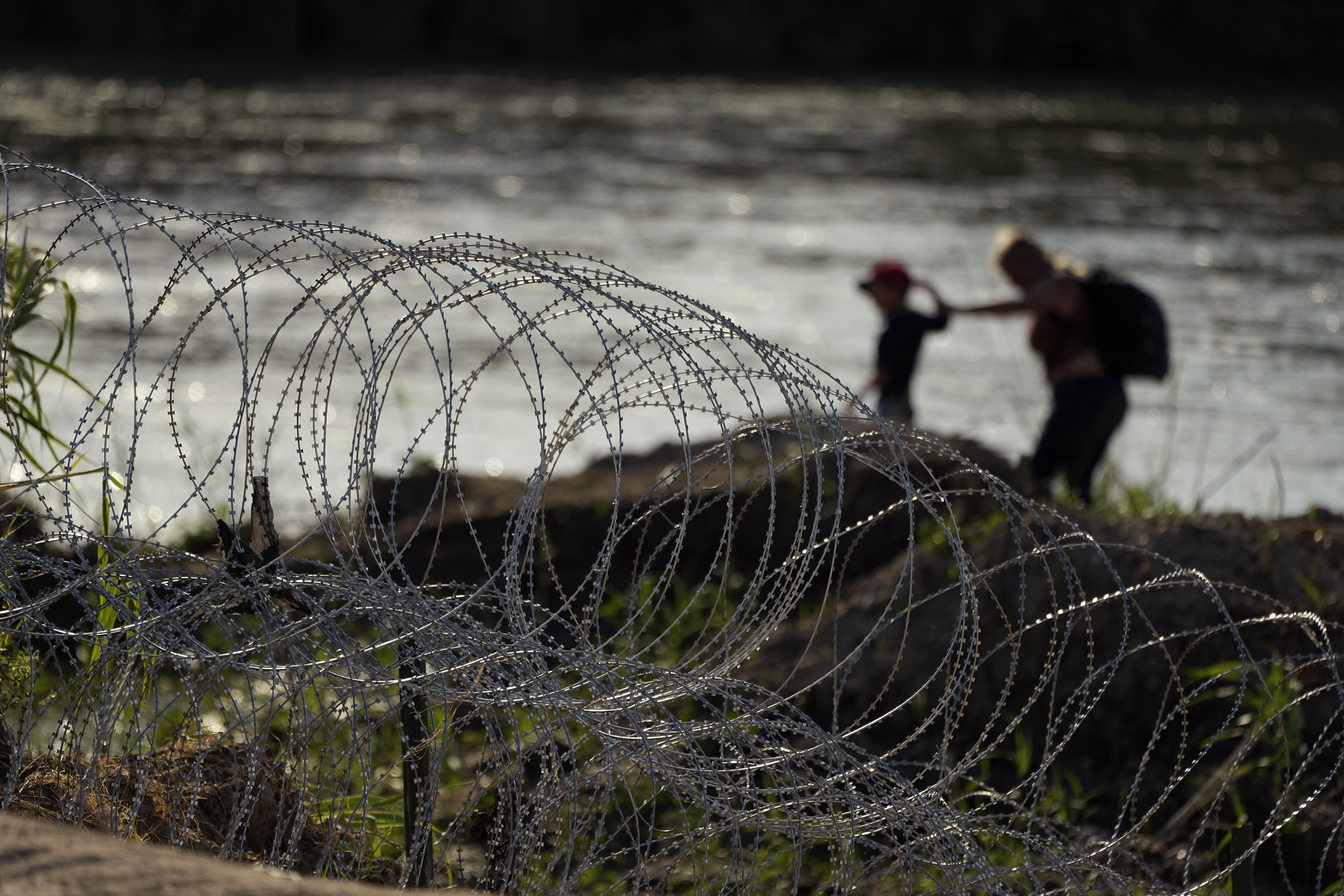Migrants walk along concertina wire as they try to cross the Rio Grande at the Texas-Mexico border ...