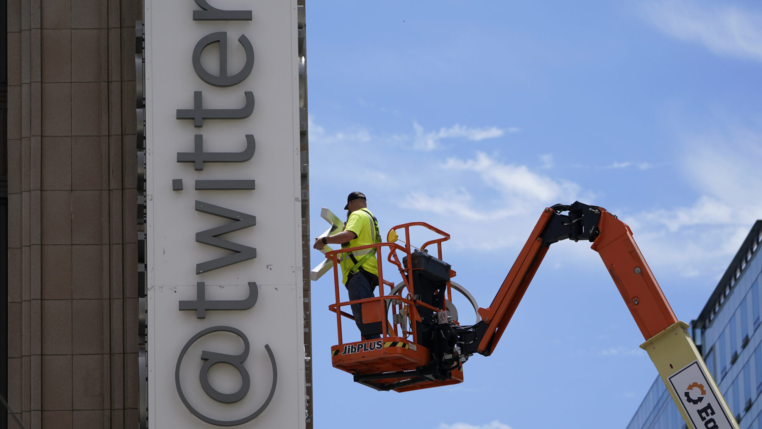 a man works on a sign that reads @twitter, musk is rebranding twitter into x...