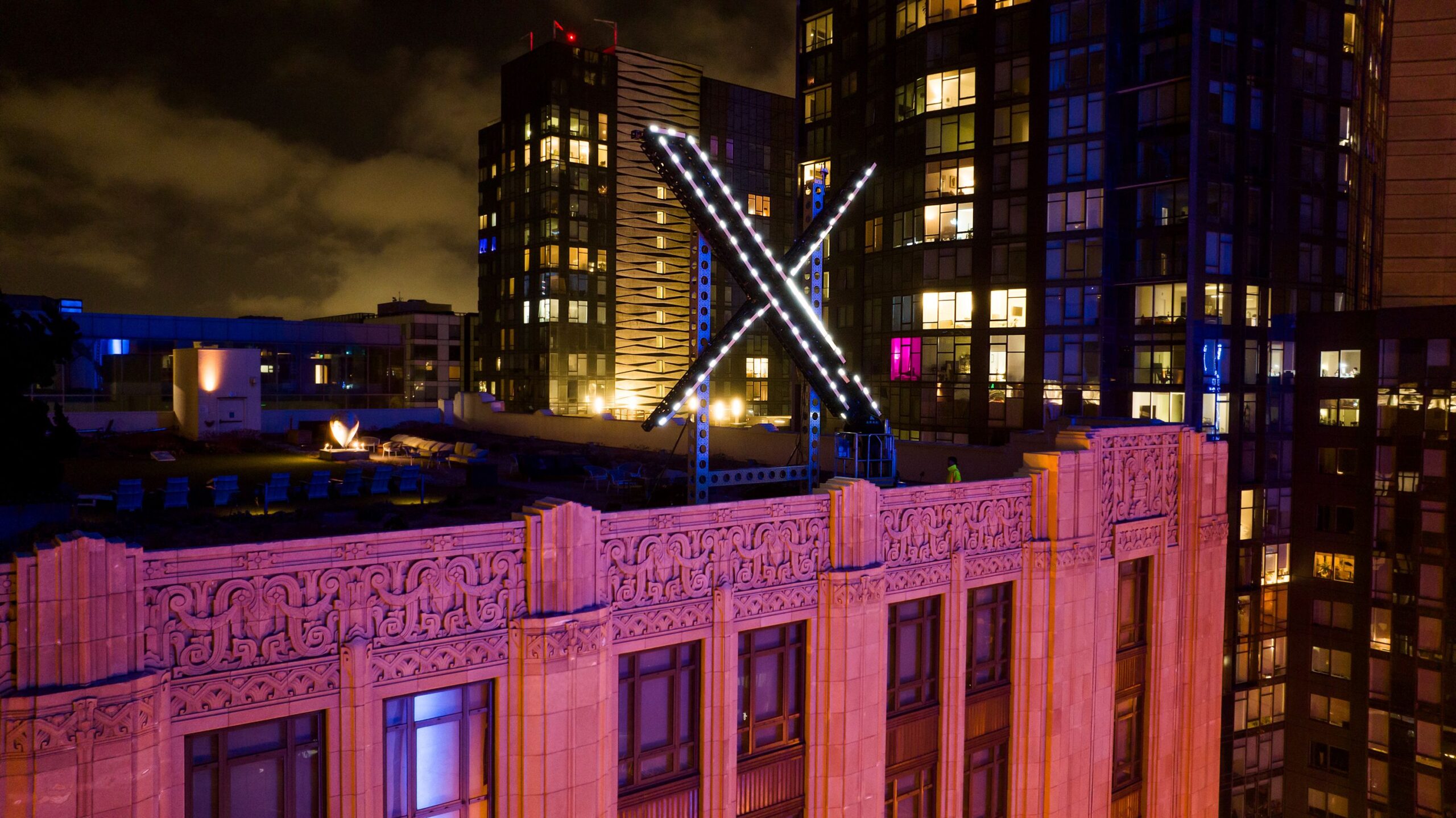 Workers install lighting on an "X" sign atop the company headquarters, formerly known as Twitter, i...