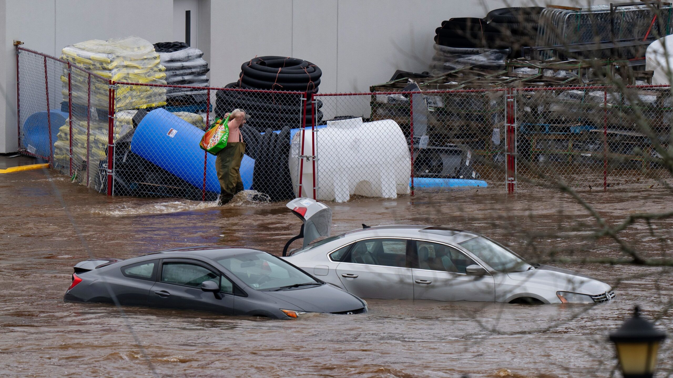 A man wearing chest waders walks past cars abandoned in floodwaters in a mall parking lot in Halifa...