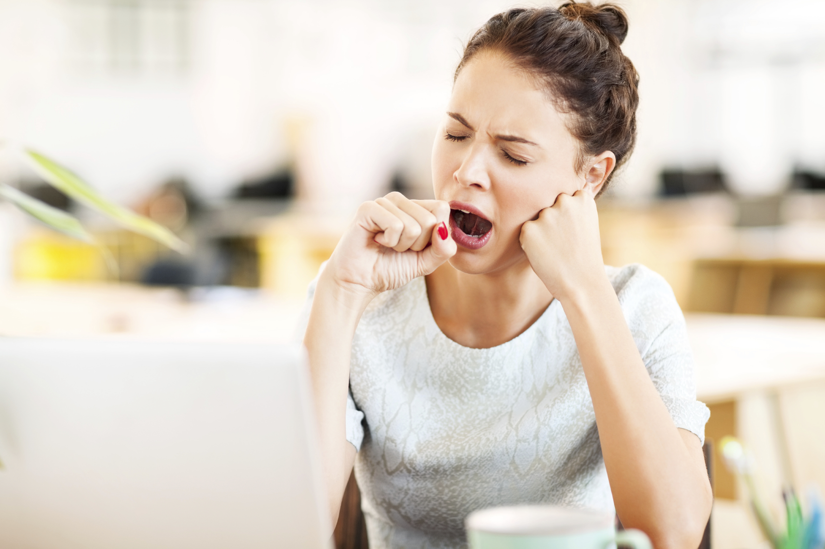 Tired woman in front of computer yawning. Creating a Sleep promoting environment is crucial to over...