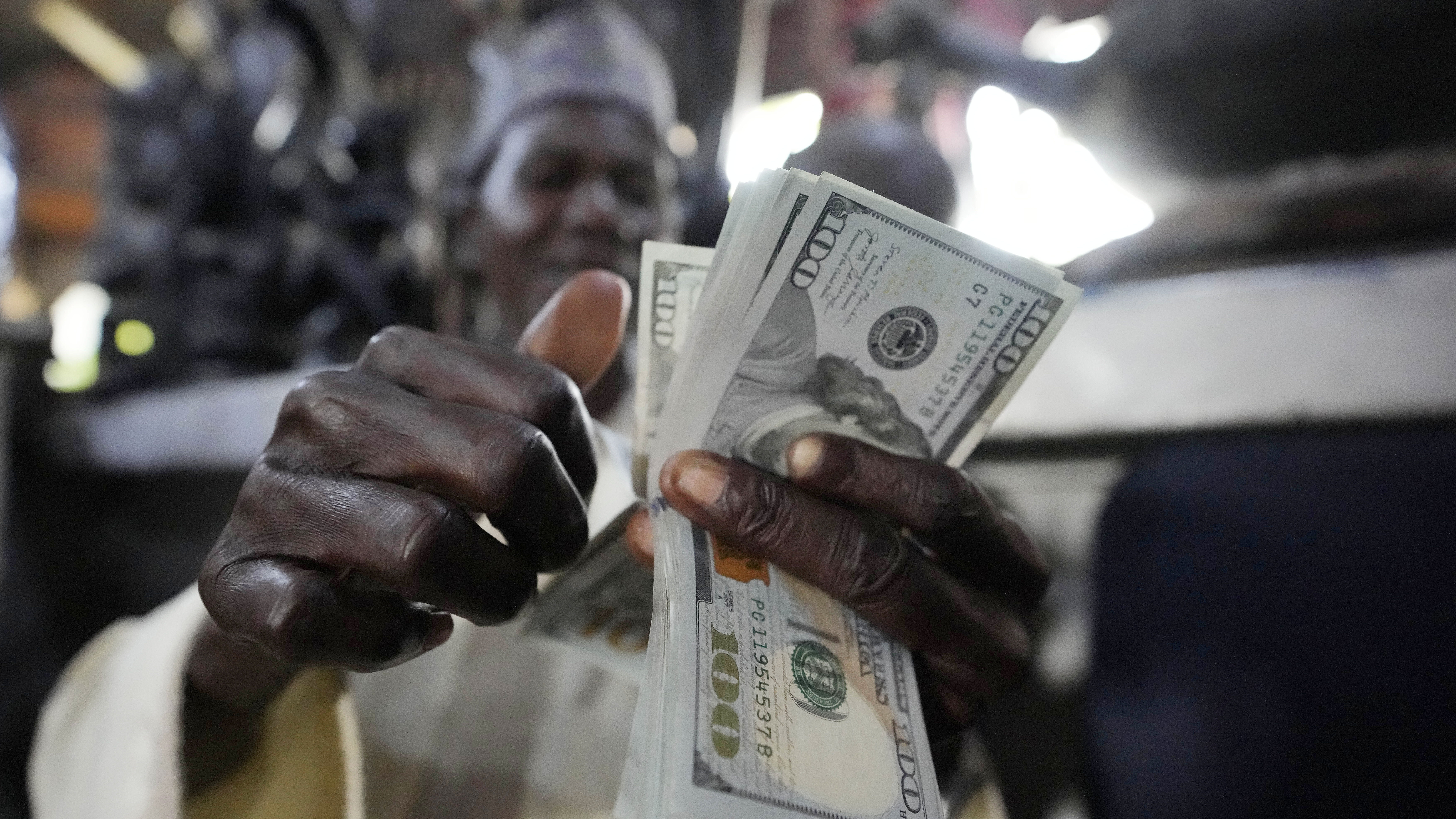 A man counts U.S. $100 bills at the craft and art market in Lagos, Nigeria, on Wednesday, Aug. 16, ...