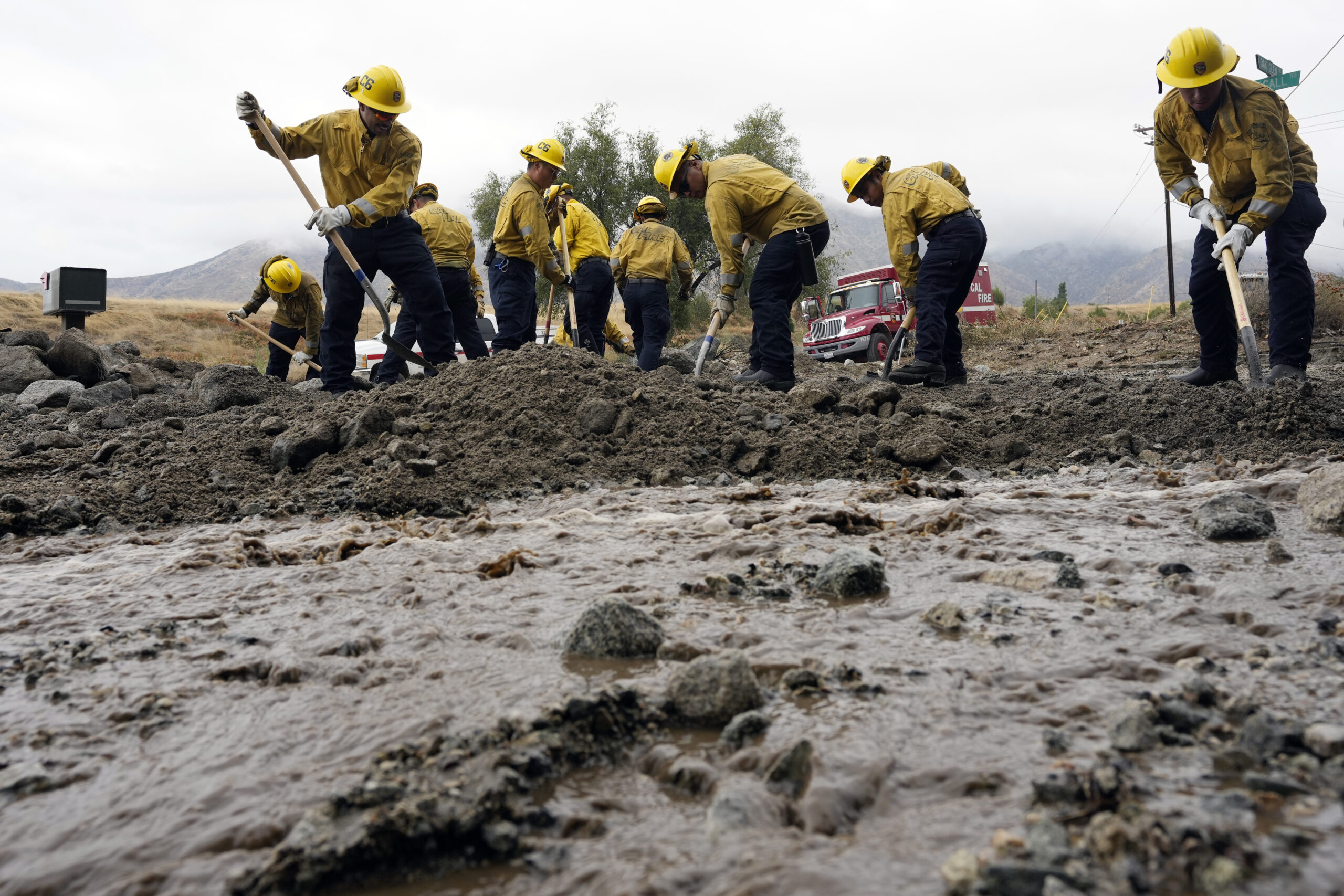 Members of Cal Fire Pilot Rock 6 crew, out of Crestline, Calif., clear mud off the side of the road...