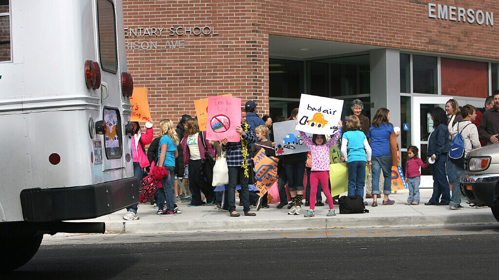 Emerson Elementary students stand outside with signs, encouraging parents to turn off their cars wh...