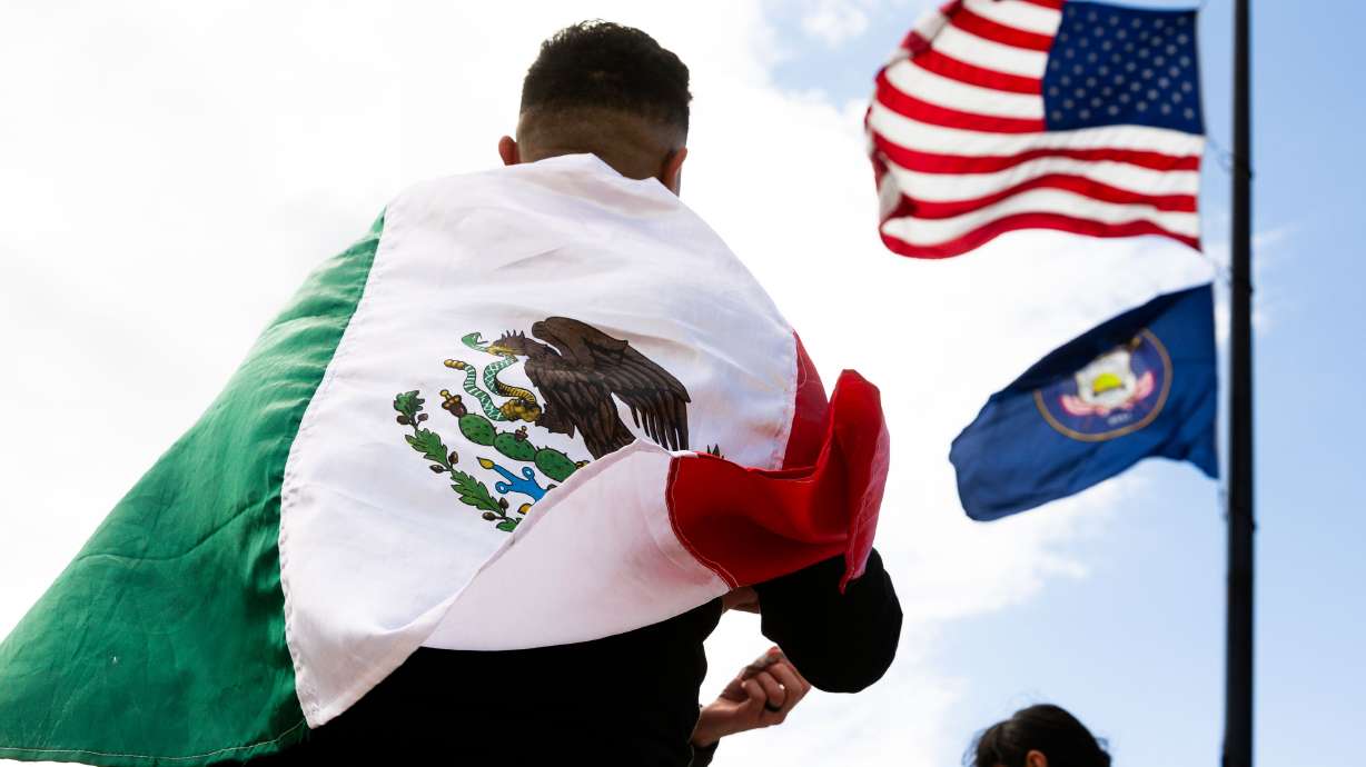 The American flag waves above an attendee wrapped in the Mexican flag at the "I Stand With All Immi...