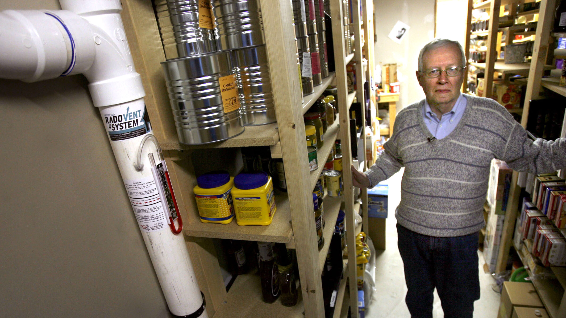 In a basement stocked with emergency food supplies Charlie McQuinn, 71, shows the radon mitigation ...
