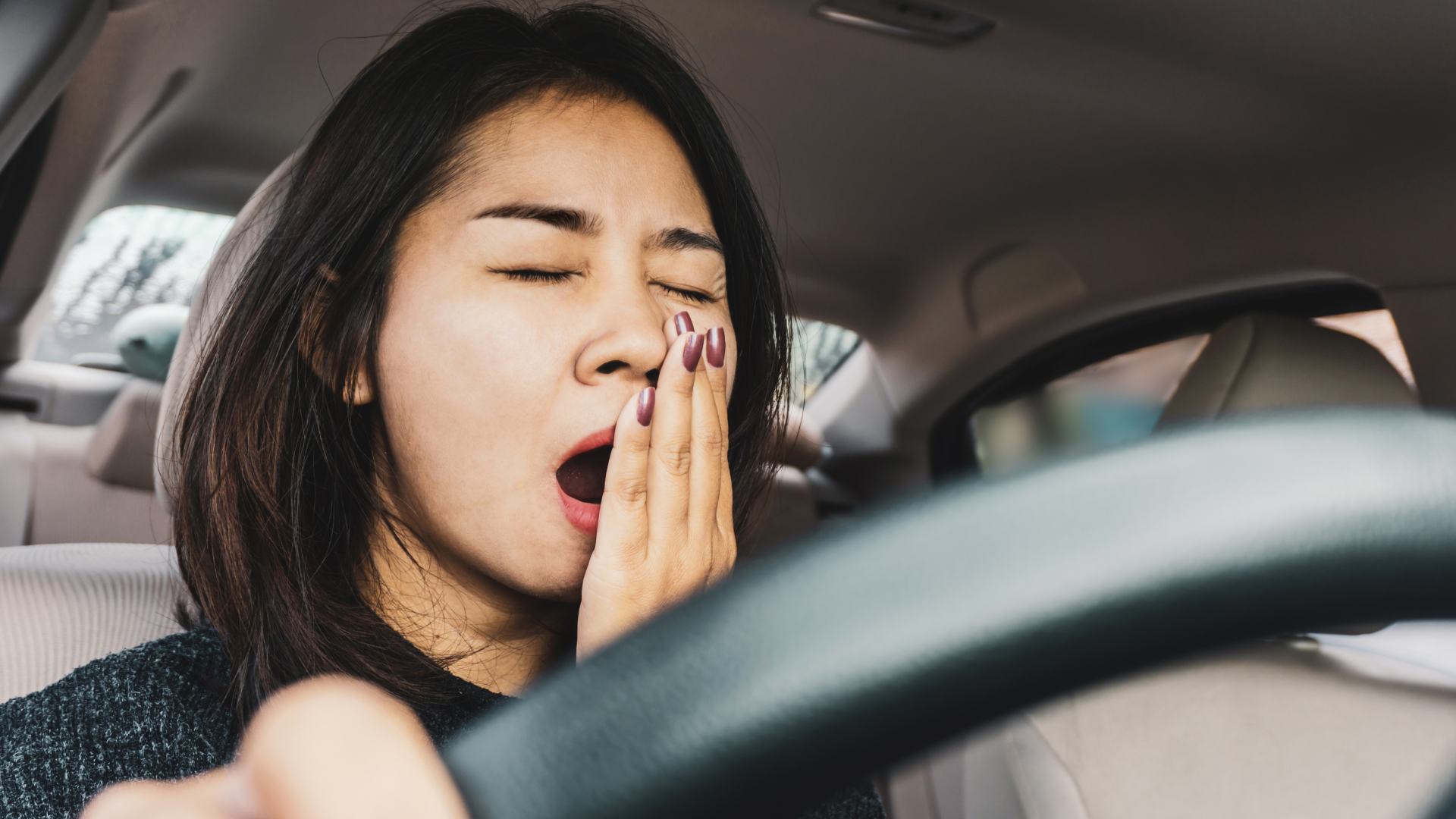 a woman yawns while driving a car...