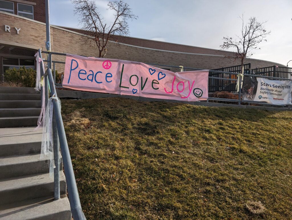 A banner outside of the school saying “Peace Love Joy.”...