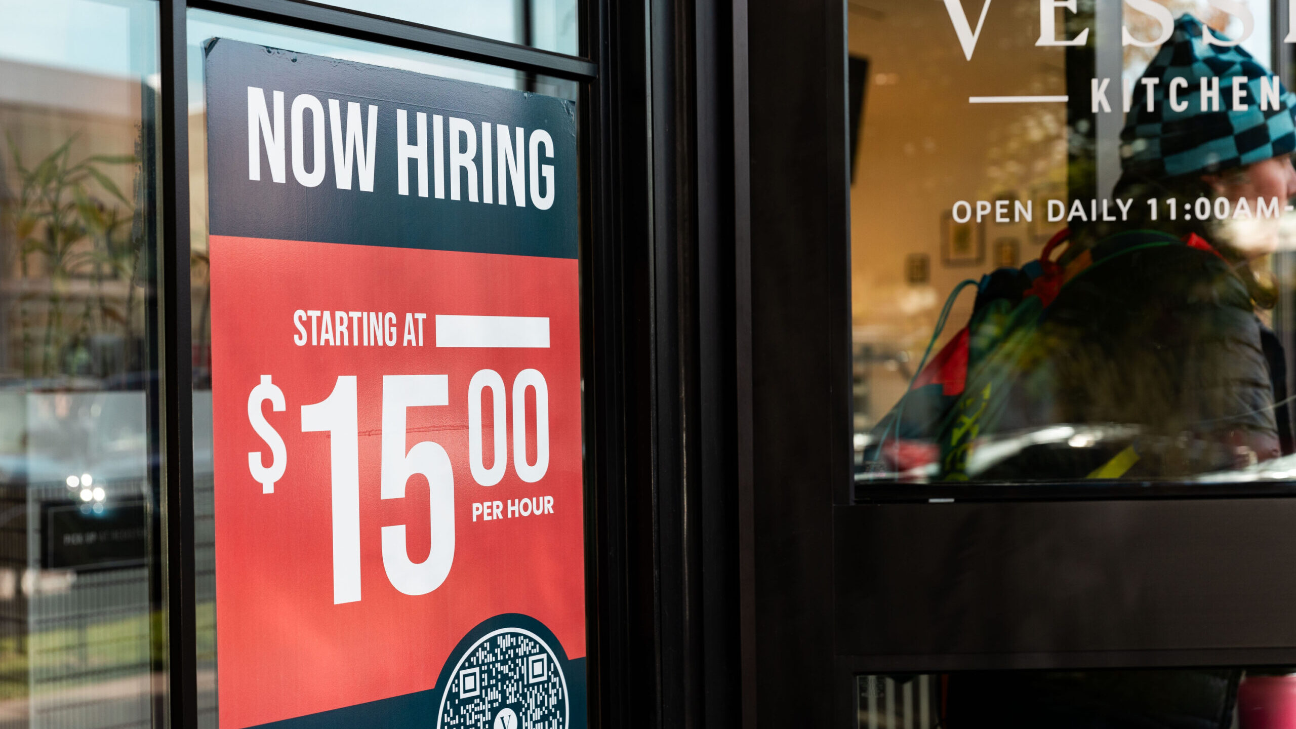 A sign reading “Now hiring” is on the window of Vessel Kitchen, utah minimum wage is at center ...