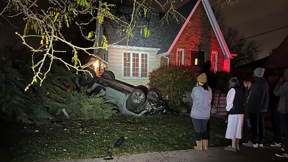 A green SUV on its roof in the front yard of a house after crashing into two parked cars and rollin...
