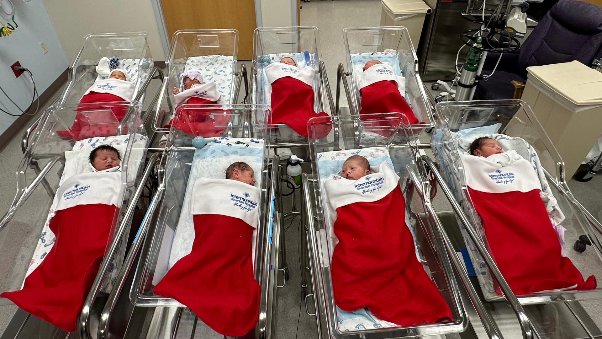 Eight babies sleep in red stockings at an Intermountain Health NICU....