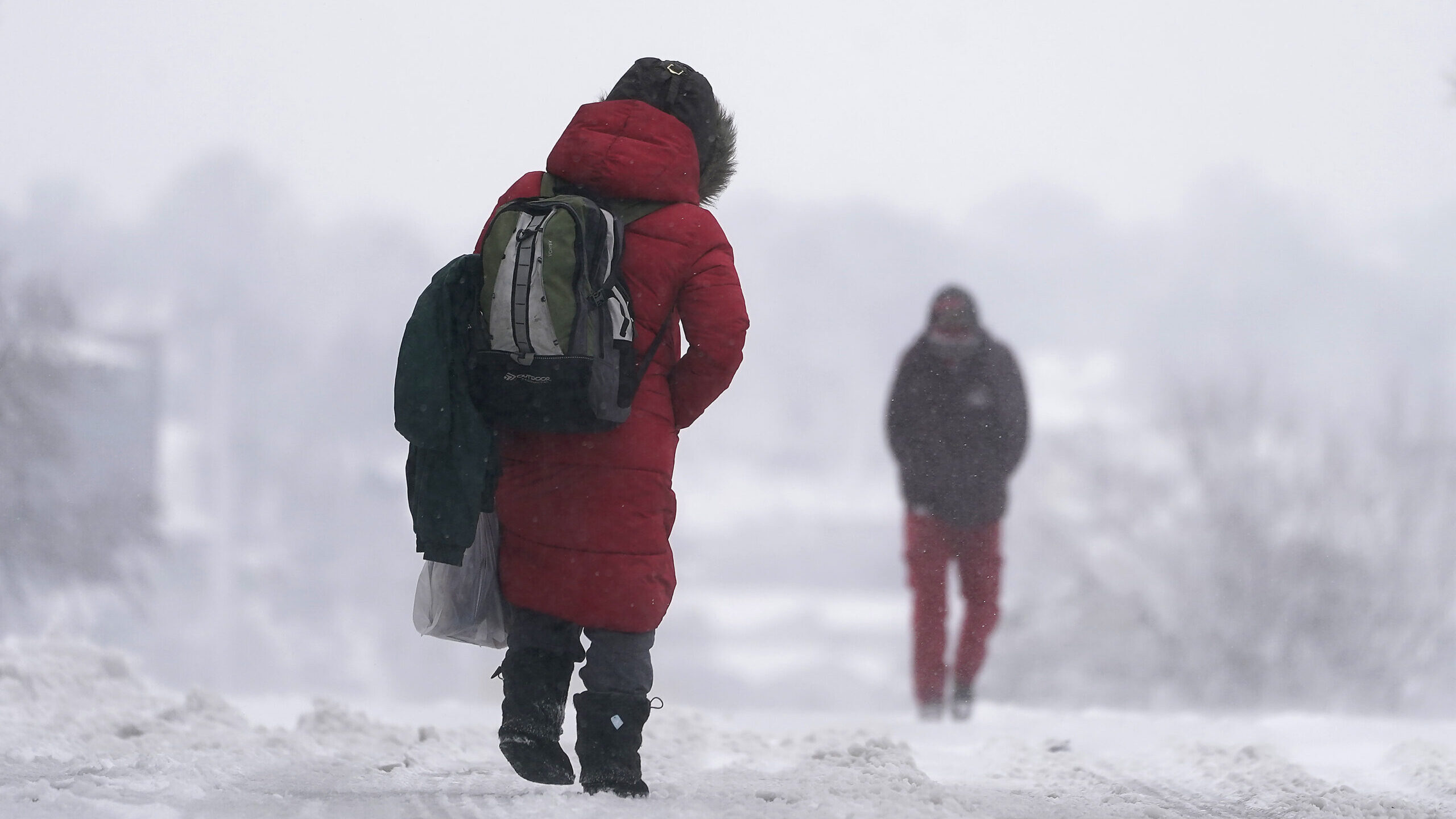 People walk down a snow-packed street as a winter storm moved through the region, Tuesday, Jan. 9, ...