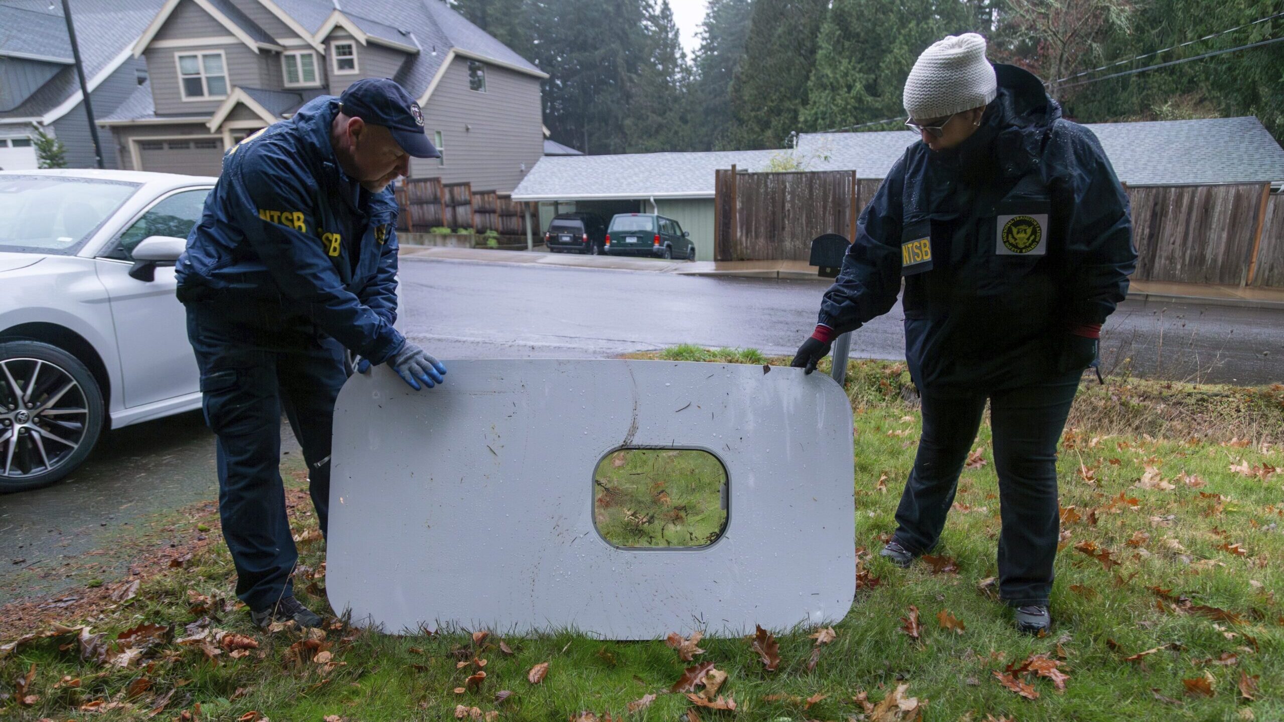 two men inspect the panel that flew off an alaska airlines plane...