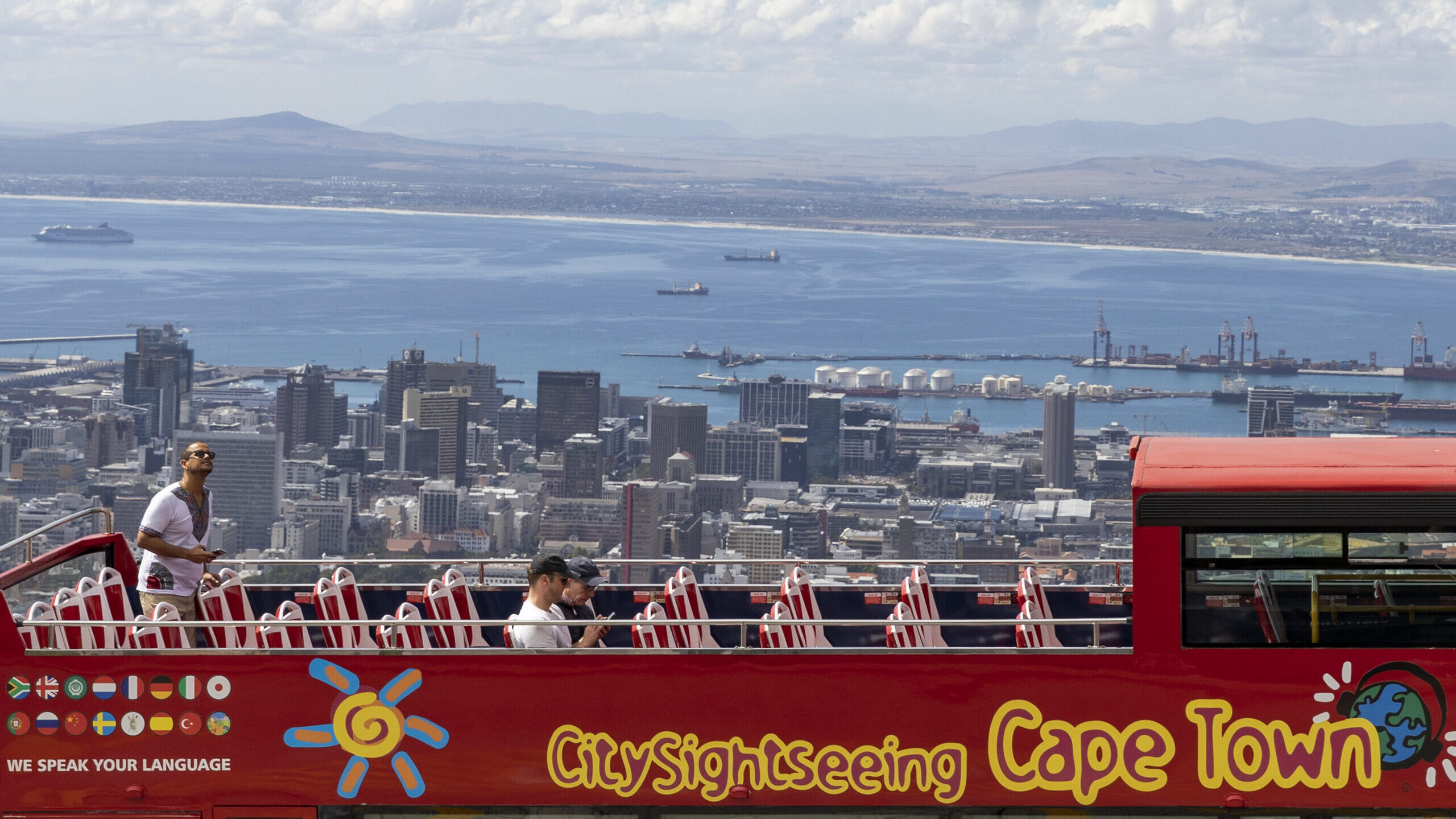 An open-air double decker sightseeing bus stops on the slopes of Table Mountain, overlooking the ci...