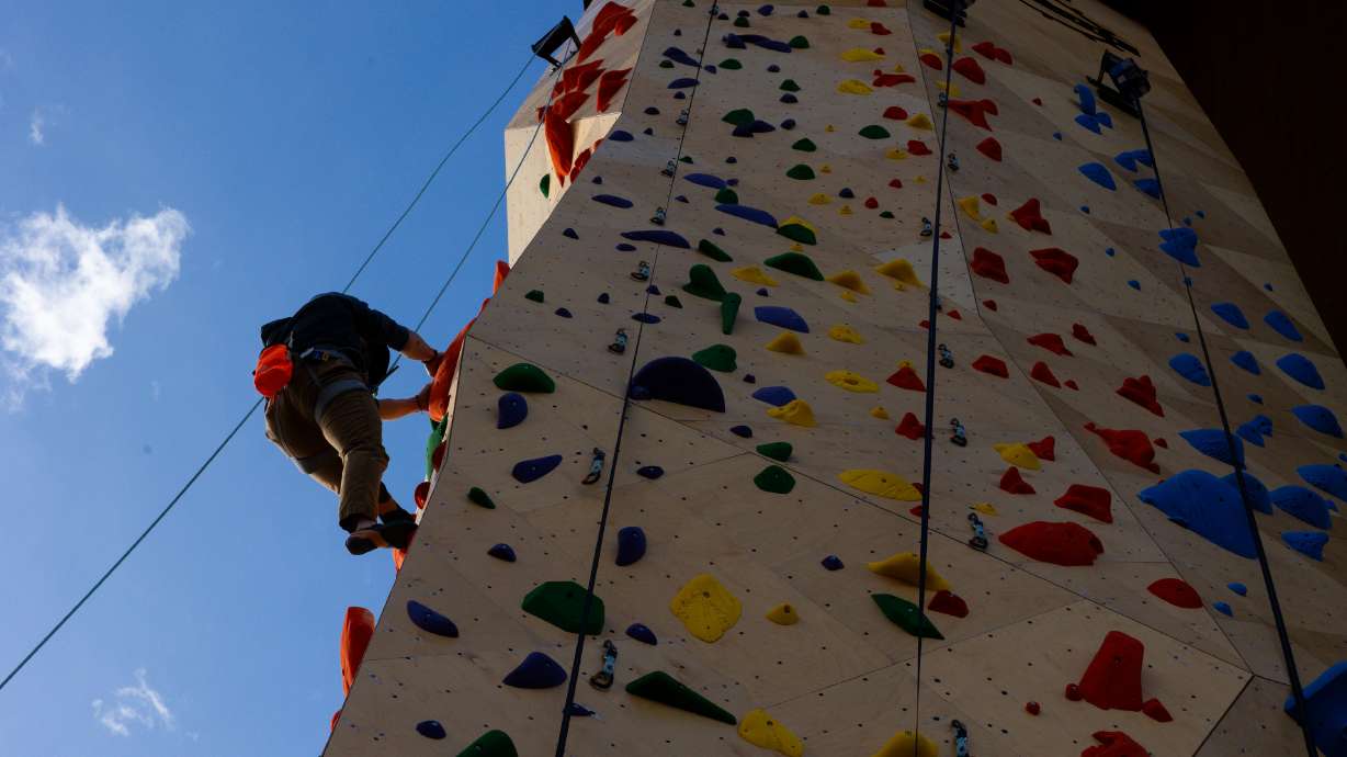 Attendees climb at the grand opening of an outdoor climbing wall outside of Millcreek City Hall on ...