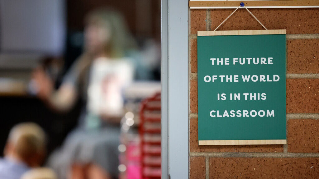 A green and brown sign hangs on a brick wall. It reads "The future of the world is in this classroo...