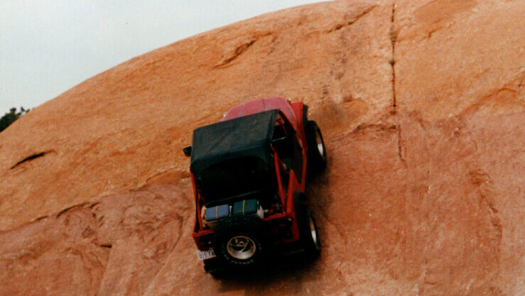 A red and black Jeep climbs up the sandy orange rocks of Moab, Utah during a Jeep safari....