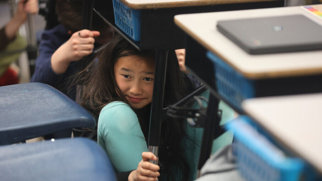 A fourth grade student sits under her desk during the 2023 Great Utah ShakeOut drill....