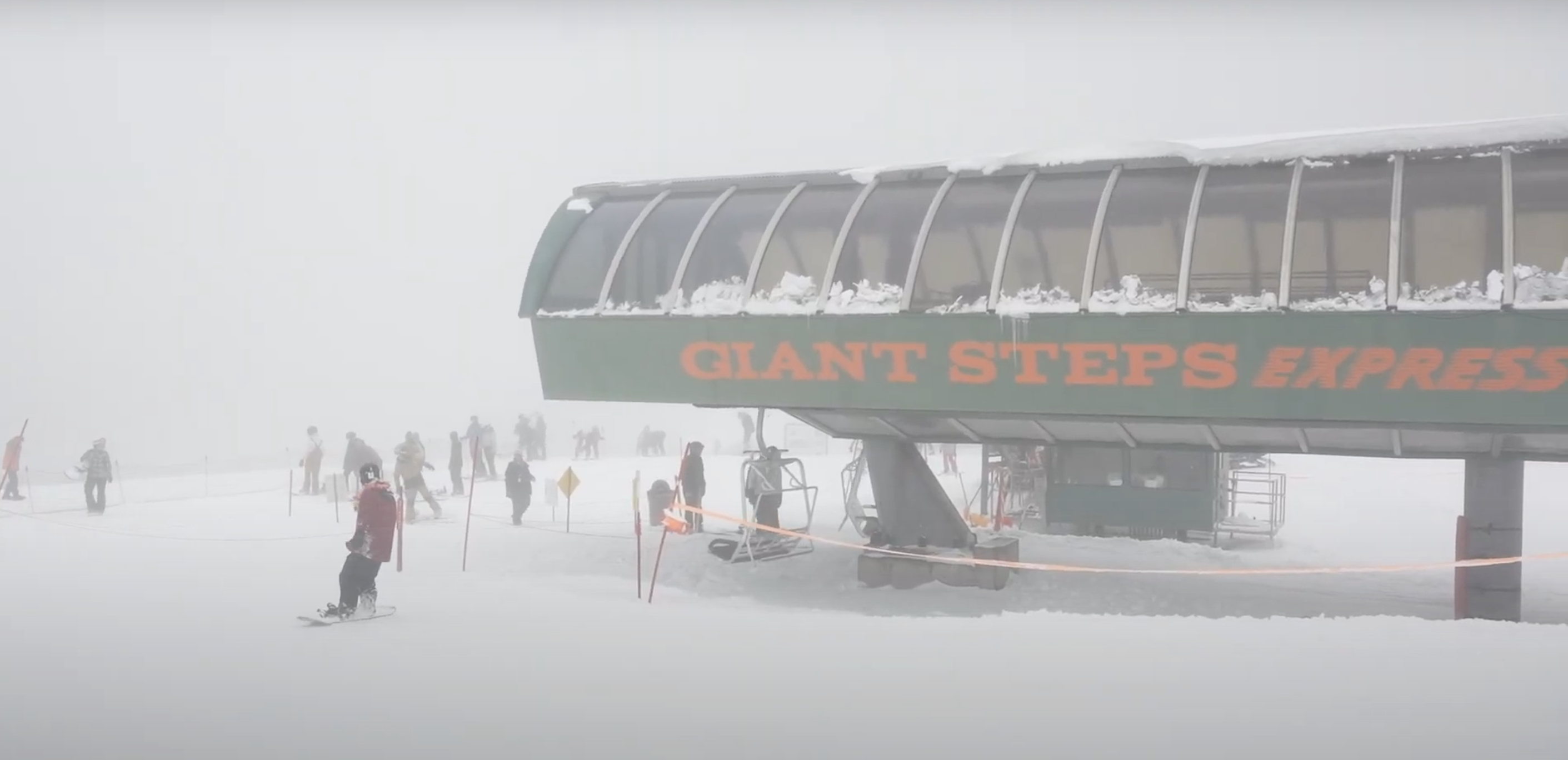 A green and orange ski lift in snowy conditions....