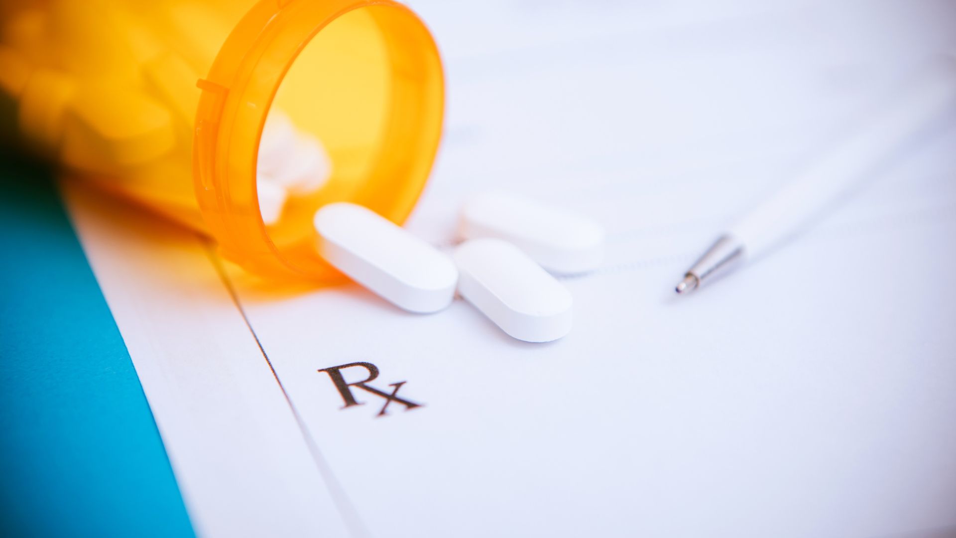 White pills spill out of an orange prescription bottle and onto a page that reads "RX"...