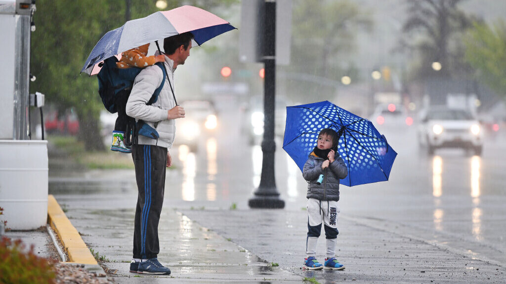 A man holds a red umbrella over himself and one of his children. A second child holds a blue umbrel...