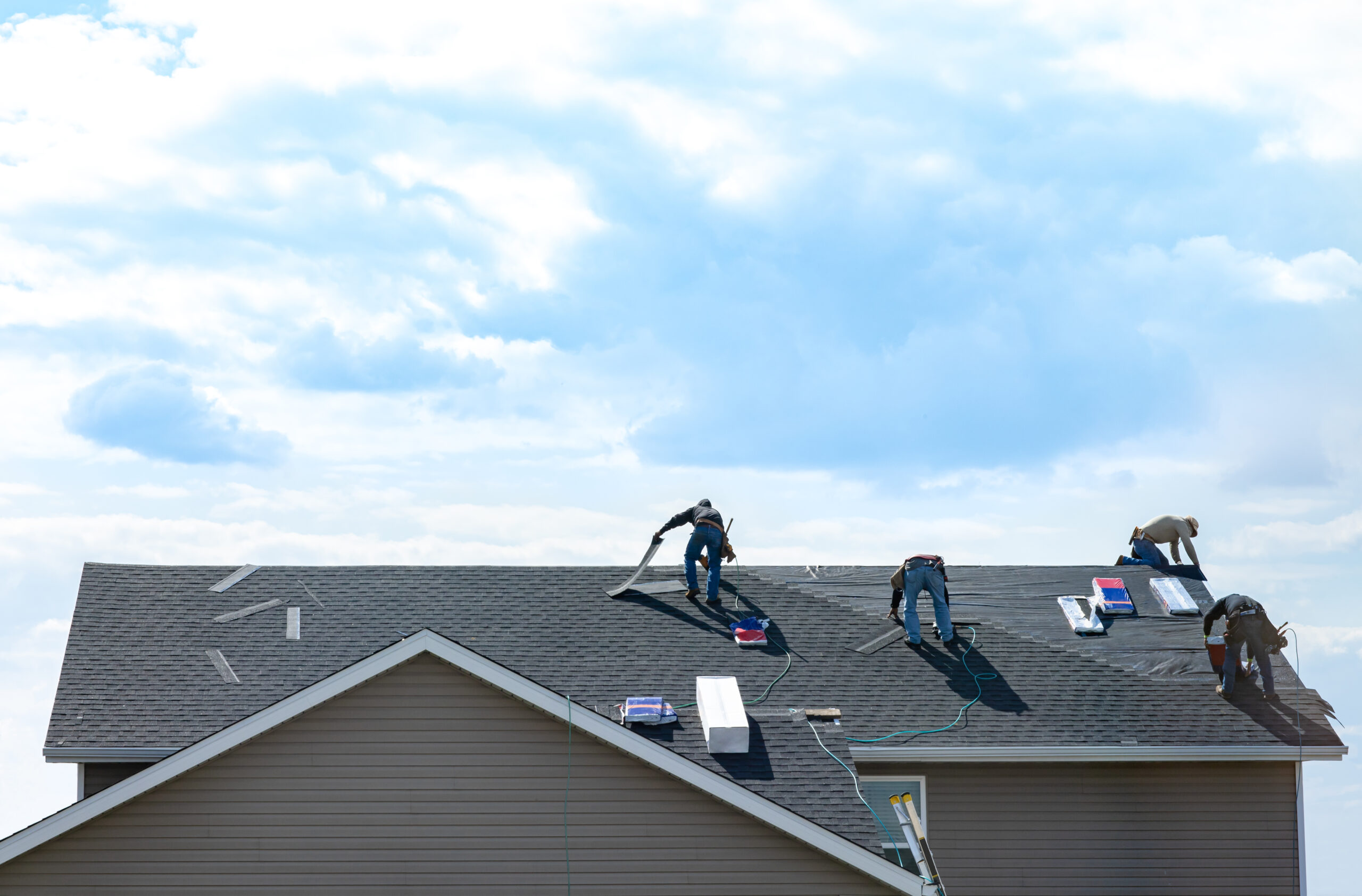 4 construction workers fixing roof against clouds blue sky, install shingles at the top of the hous...