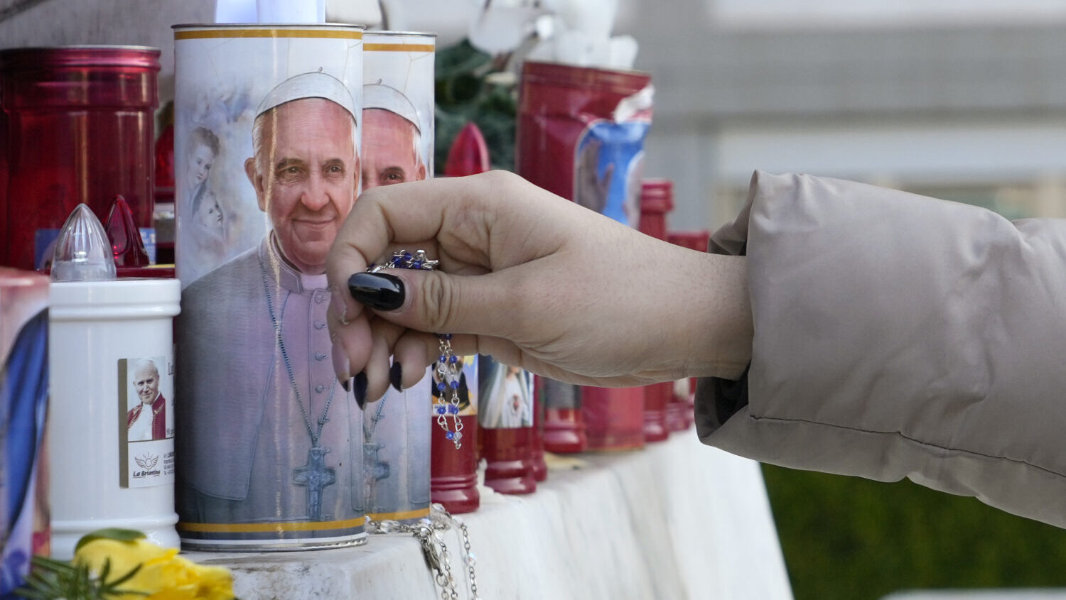 A woman lays a rosary near candles adorned with pictures of Pope Francis outside the Agostino Gemel...
