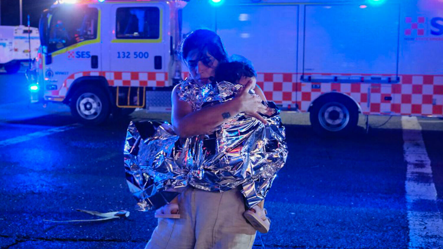 A member of the public leaves the scene with her child, who is covered in an emergency blanket, aft...