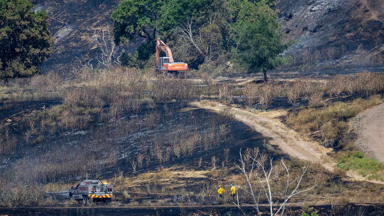 An excavator moves debris as firefighters keep watch on Tuesday of the area torched in a fire Monday in Washington Terrace. (Photo: Scott G. Winterton, Deseret News)