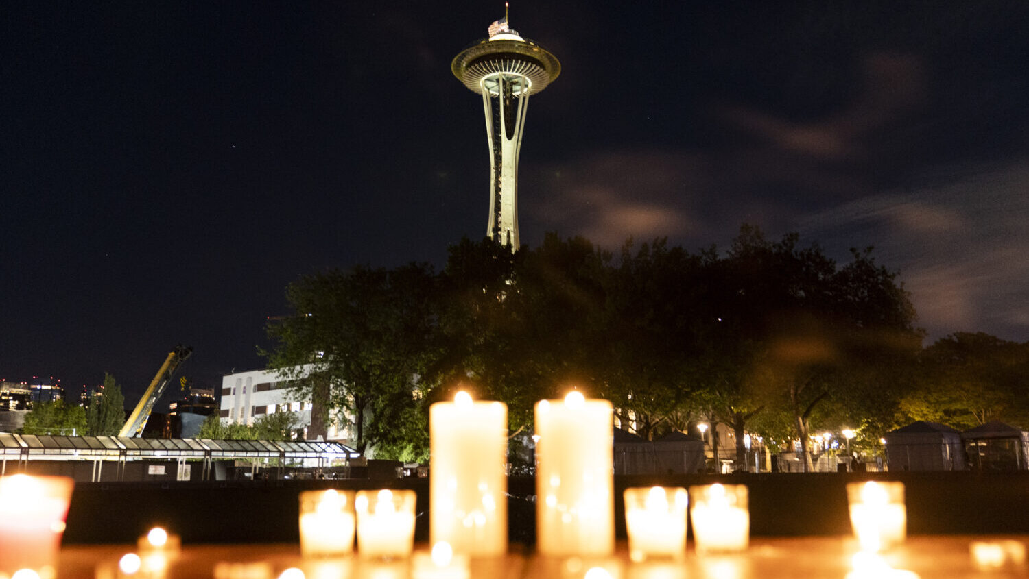 A U.S. flag is flown at half-staff atop the Space Needle as candles glow during a vigil a day after the Bite of Seattle food festival shooting at Seattle Center on July 27, 2026 in Seattle, Washington. Three people are dead and four are wounded. (David Ryder, Getty Images)