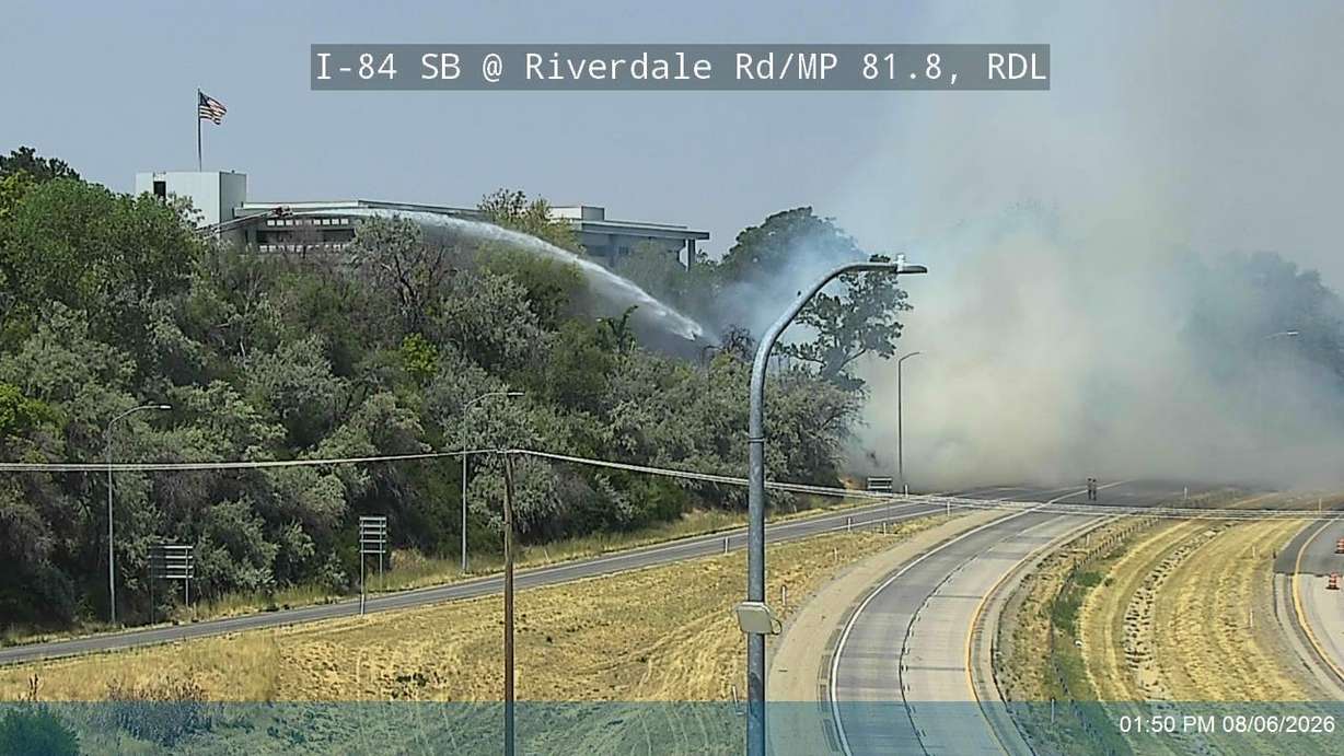 Firefighters pour water on a fire that threatened a building along Interstate 84 on Thursday. (Photo: Utah Department of Transportation)