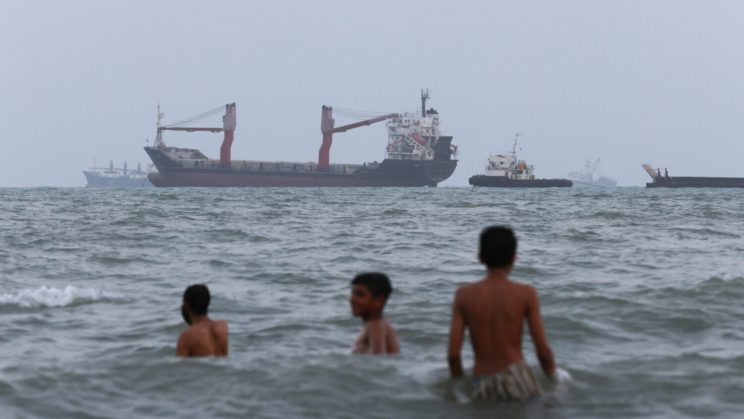 Children swim as ships are seen anchored in the Strait of Hormuz on August 10, 2026 off the coast o...